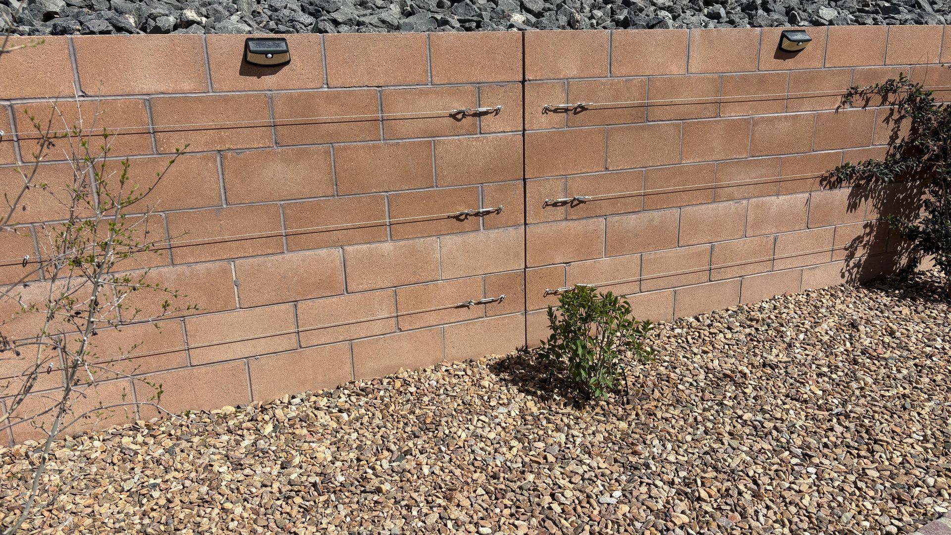 Brown block retaining wall with gravel and small plants.