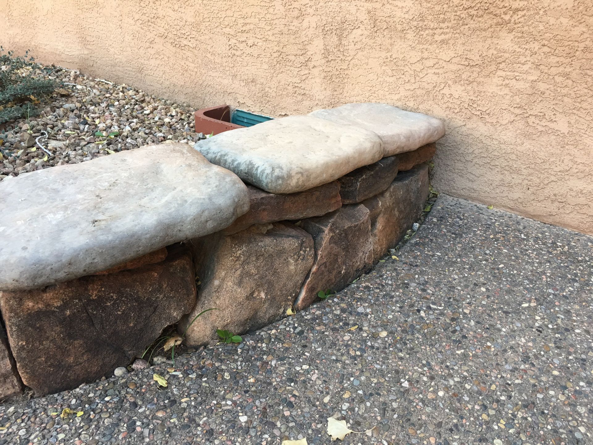 Stone wall with three large, flat rocks on top for seating against a stucco wall.