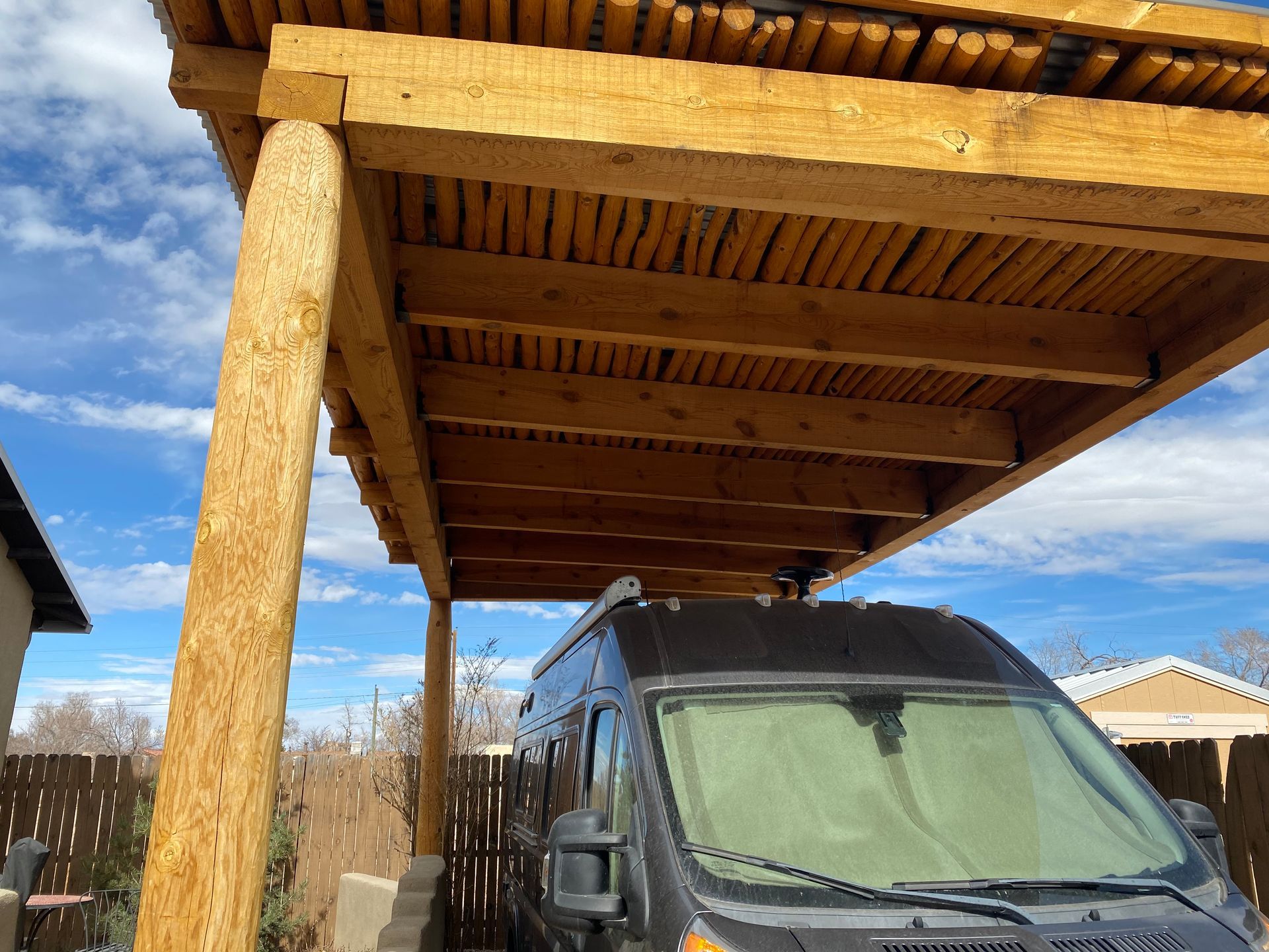 A black van parked under a wooden carport with a blue sky backdrop.