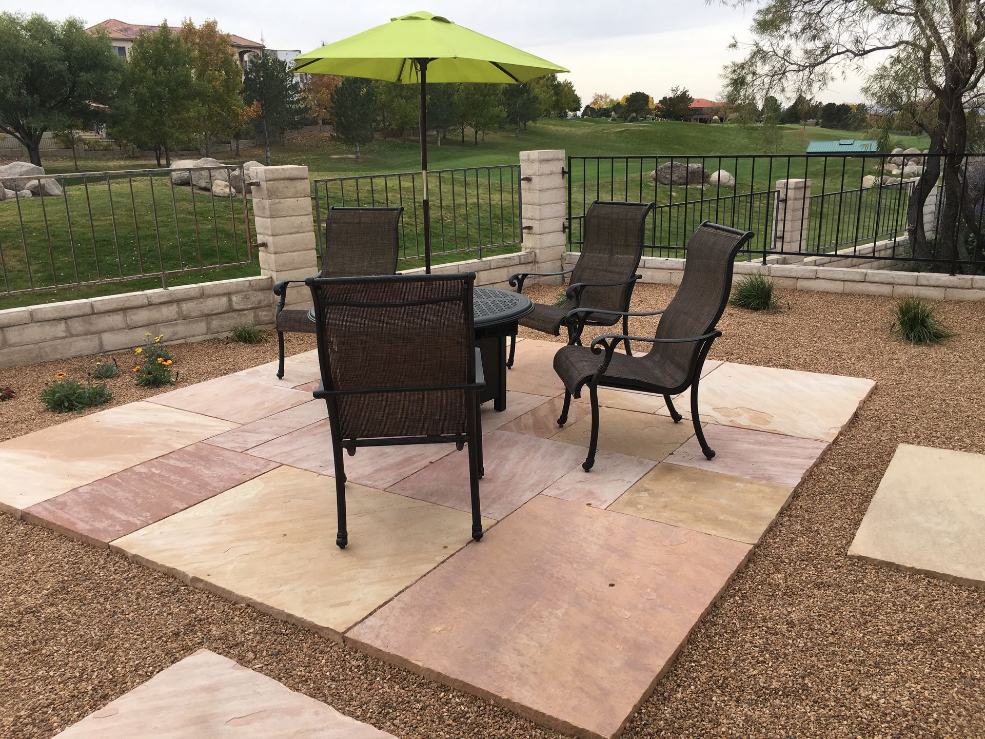 Patio with table and chairs, green umbrella, and surrounding landscaping.