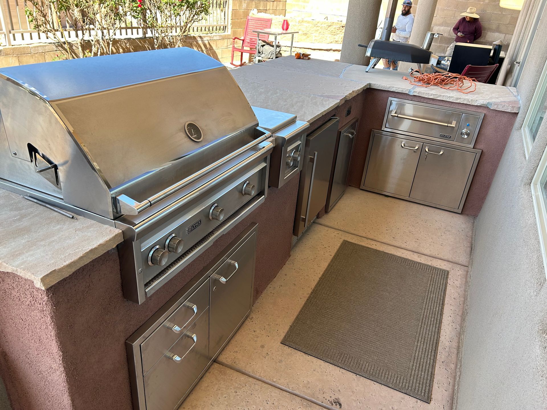 Outdoor stainless steel grill and built-in kitchen in a backyard setting.