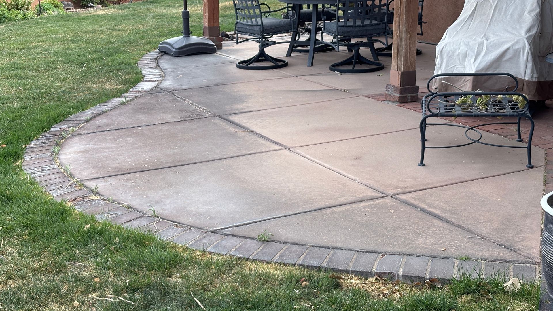 Concrete patio with a brick border next to green grass. Outdoor setting with furniture.