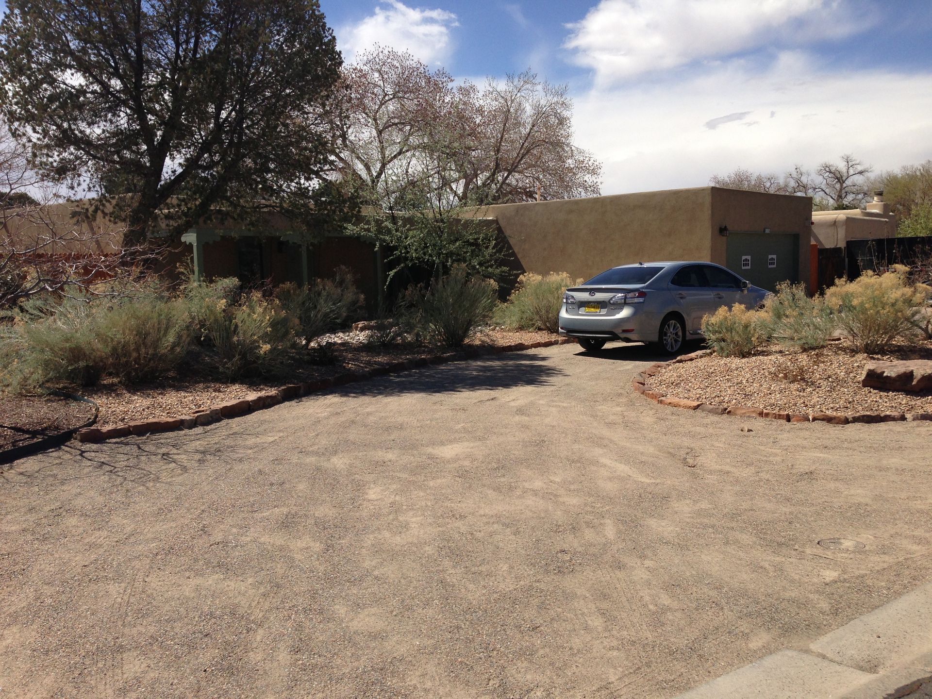 A gray car parked in a gravel driveway in front of a tan stucco building with desert landscaping.