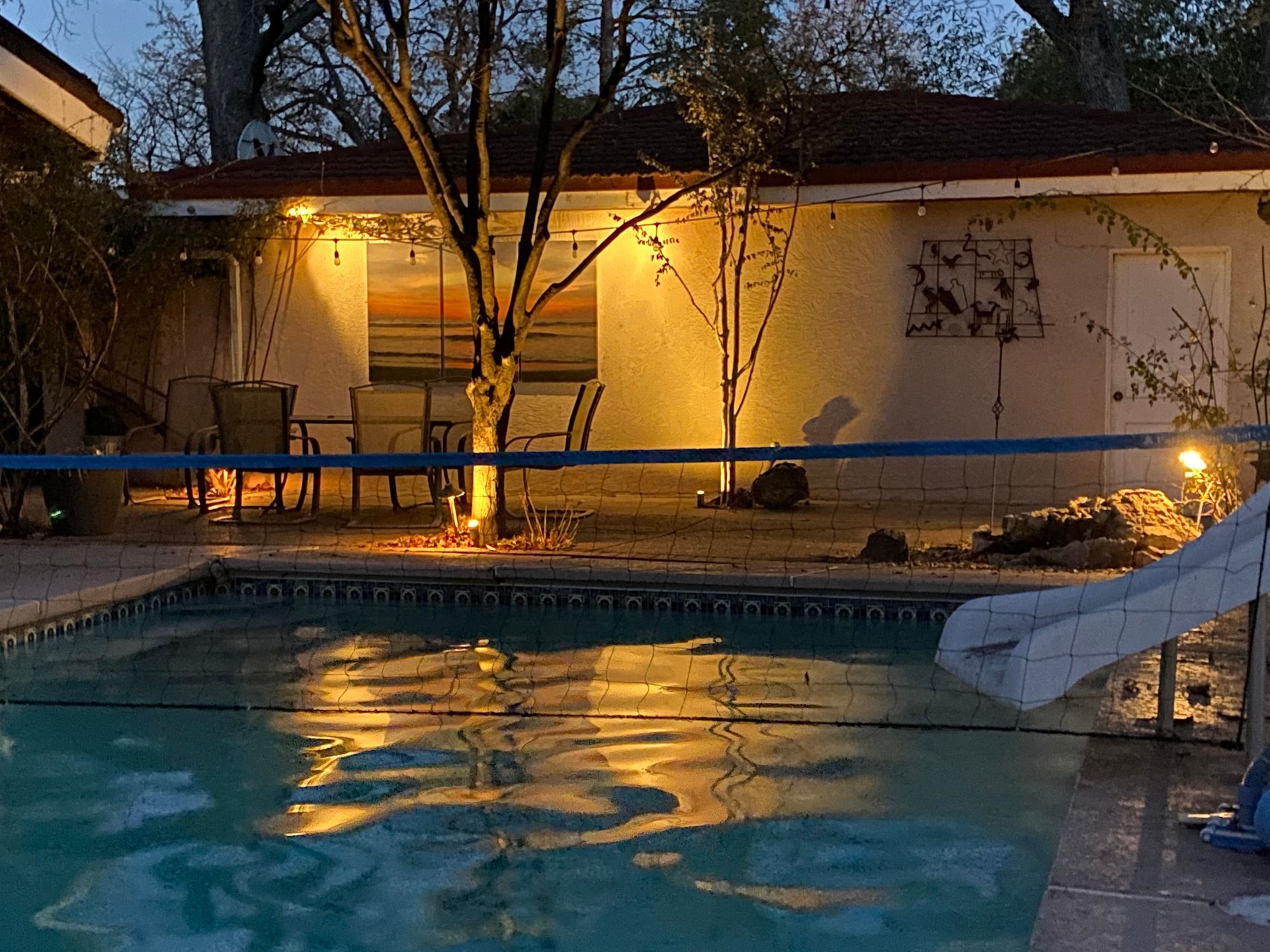 Pool at night with illuminated house, chairs, and a slide.