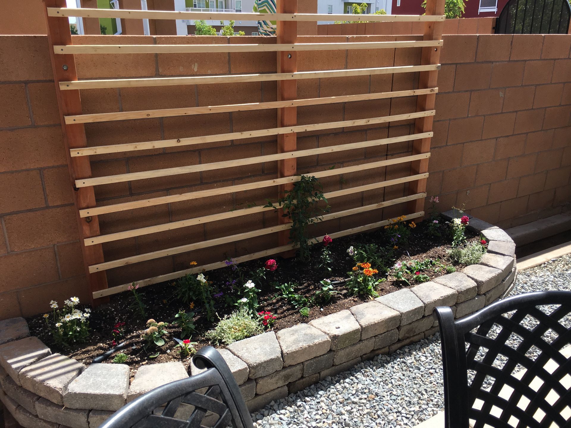 A wooden lattice on a cinder block wall over a flower bed with colorful flowers.