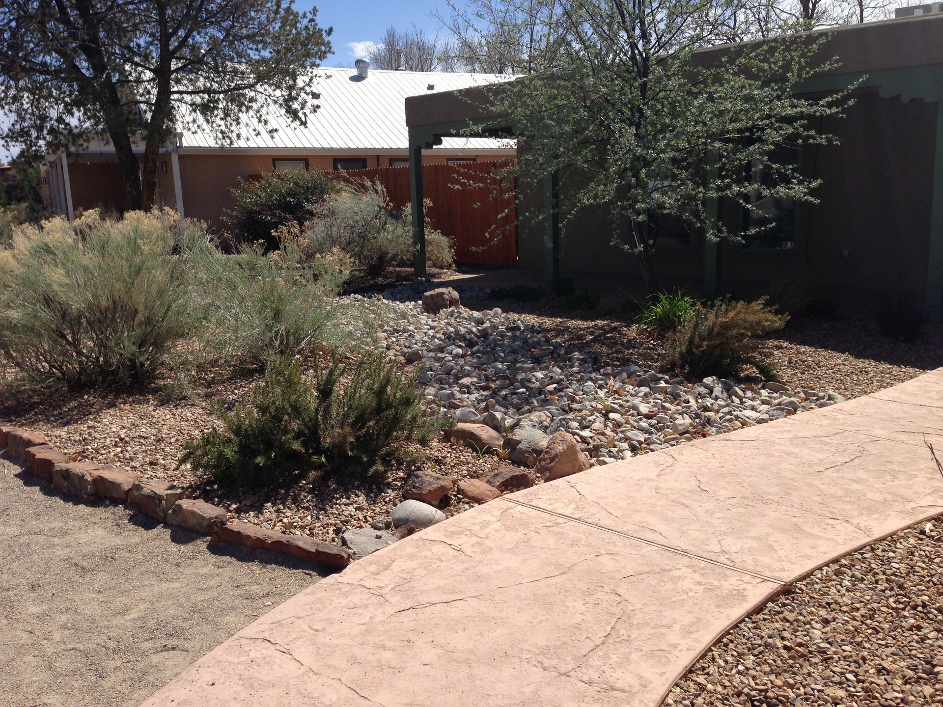 Curved walkway leading to a rock and plant-filled yard, with a building in the background.