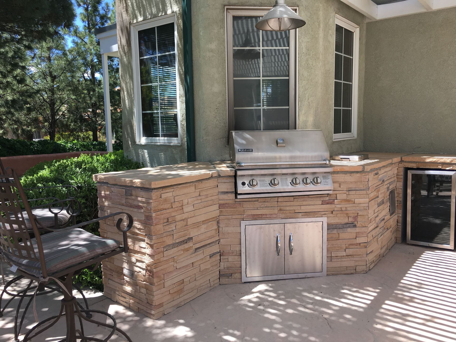 Outdoor kitchen with stone veneer, grill, stainless steel appliances, and a bar stool.