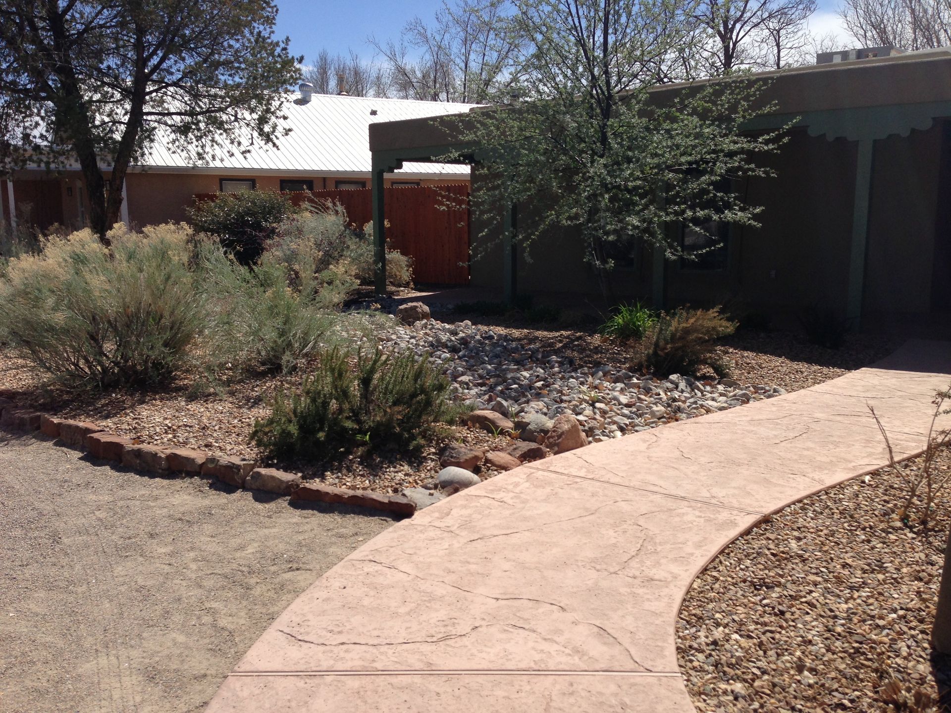 Curving stone pathway leads to a house with desert landscaping, including bushes, rocks, and a gravel ground cover.