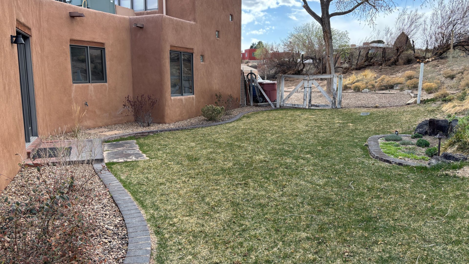 Exterior of a terracotta-colored building with a small yard and gravel landscaping; blue sky.