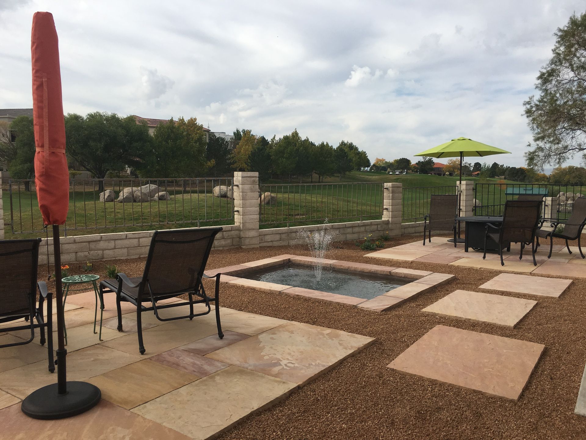 Patio with seating, fountain, and umbrella; background of trees and cloudy sky.