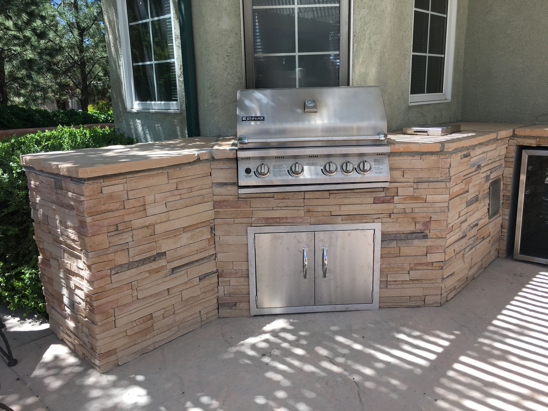 Outdoor kitchen with a stainless steel grill and stone facade.