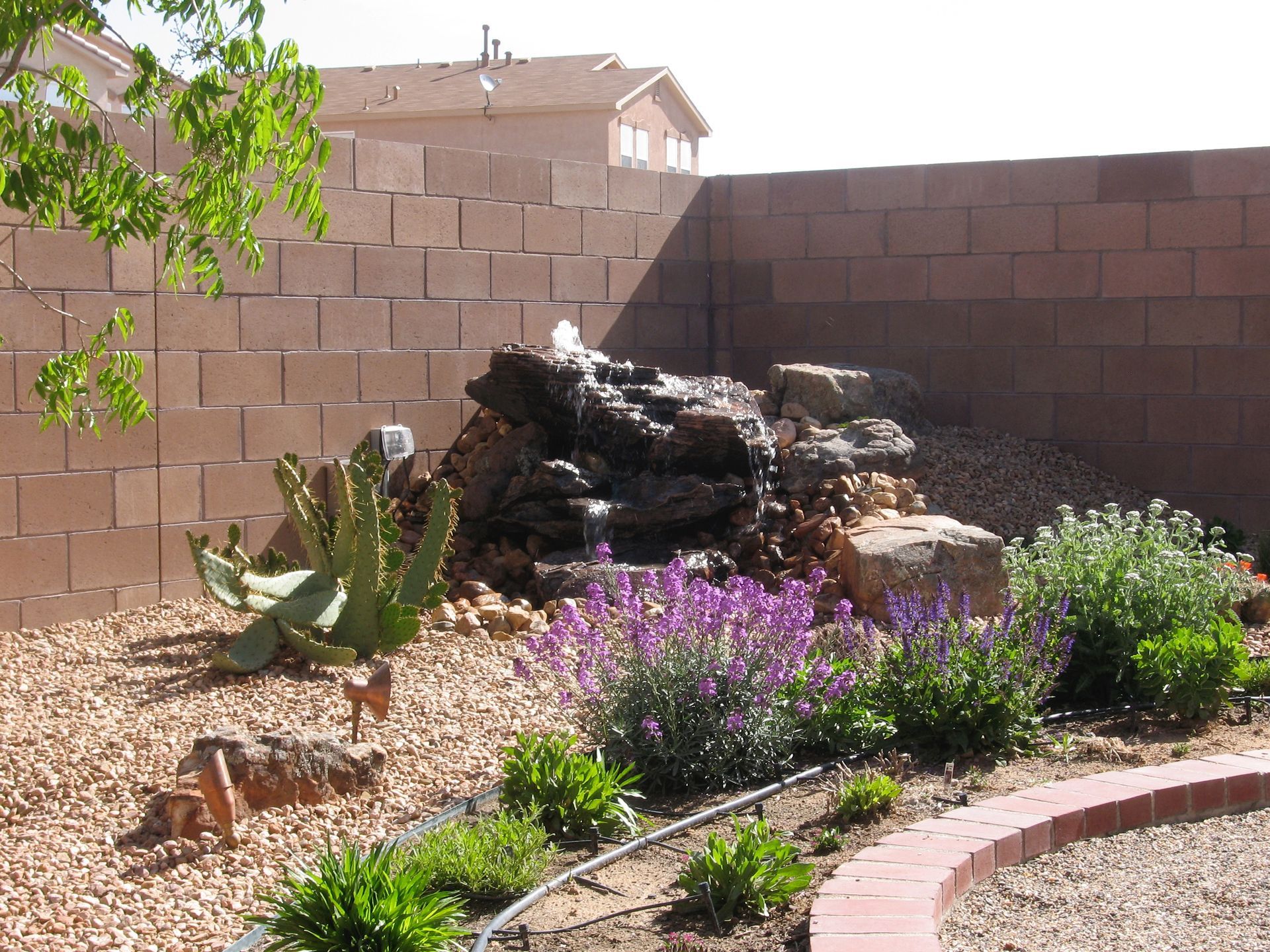 Backyard with rock fountain, plants, and a brick wall.
