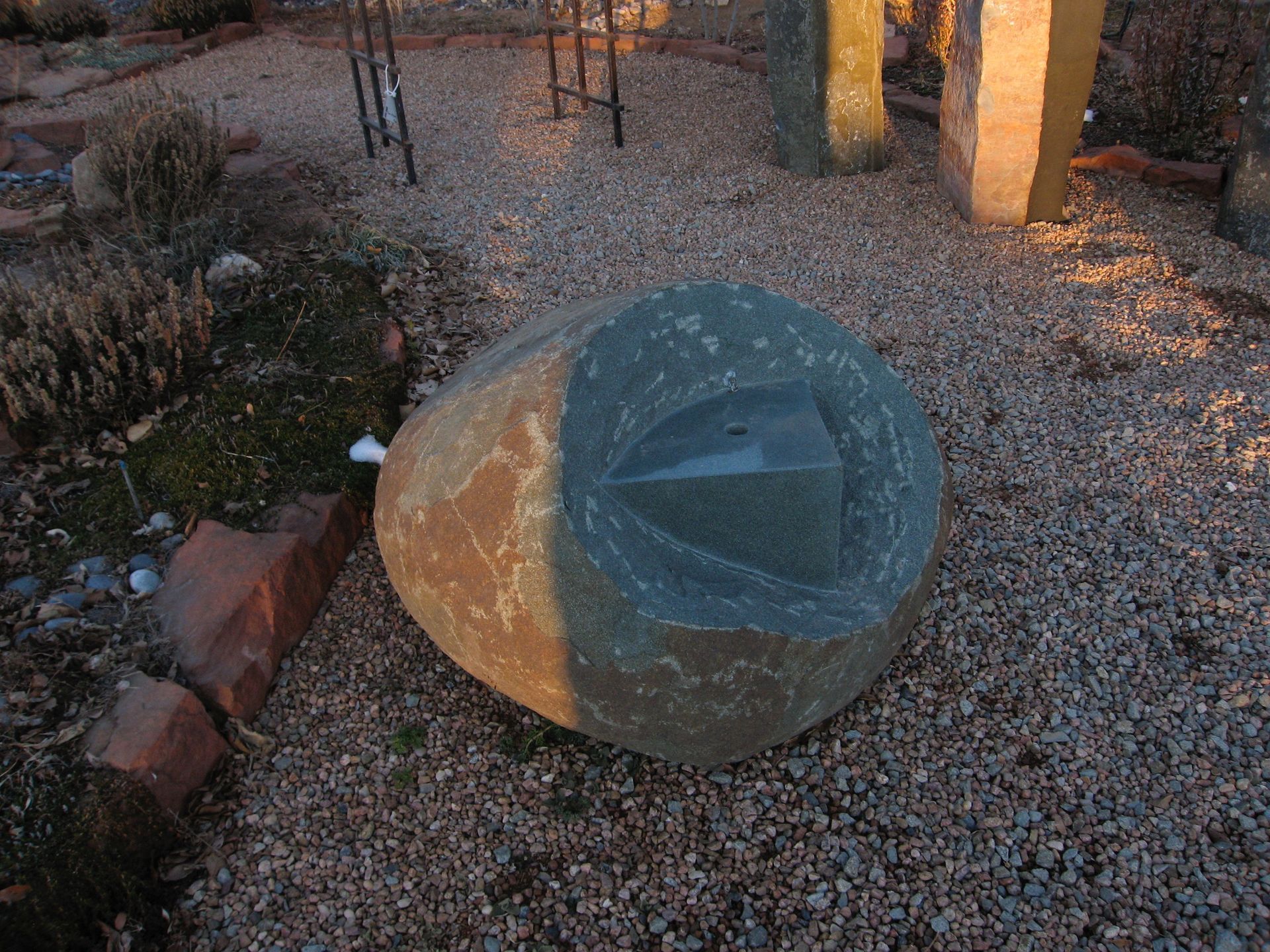 Stone sculpture with a carved triangle in a gravel garden setting.