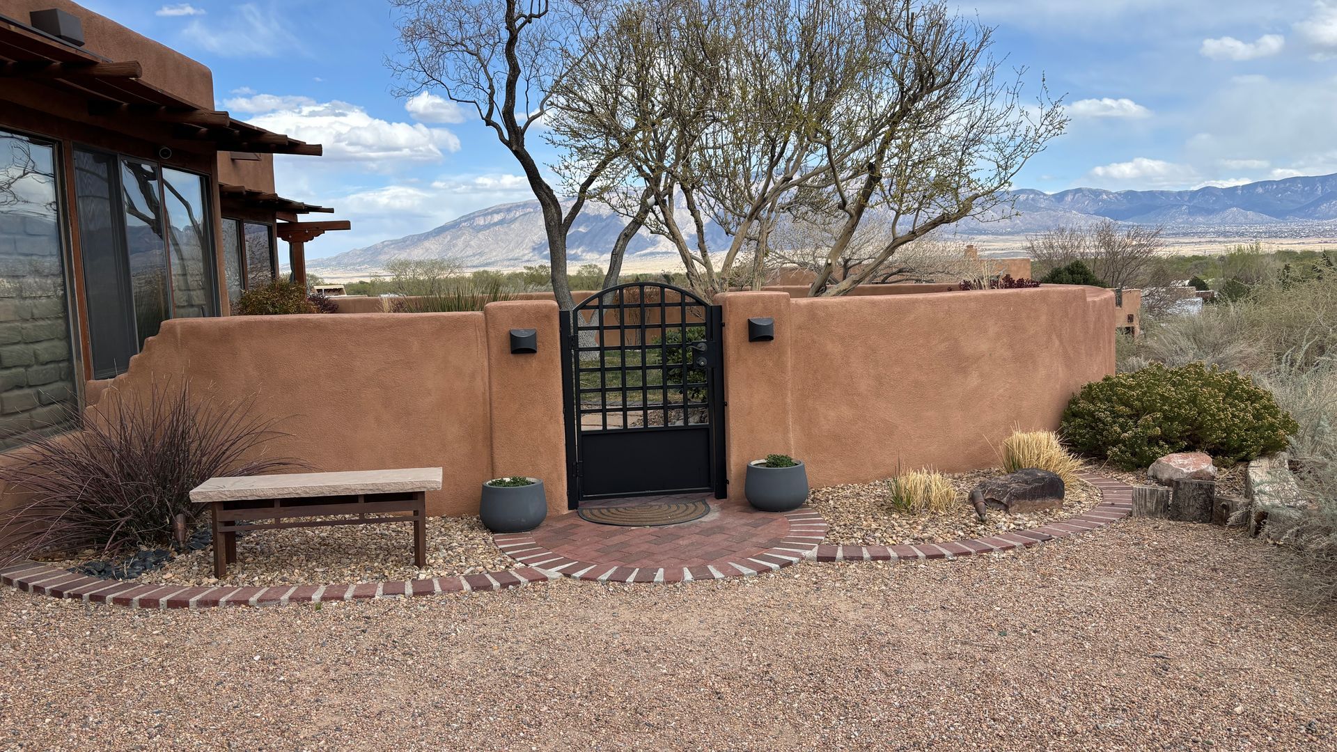Exterior view of a Southwest-style home with a terracotta wall, black gate, bench, and desert landscaping.