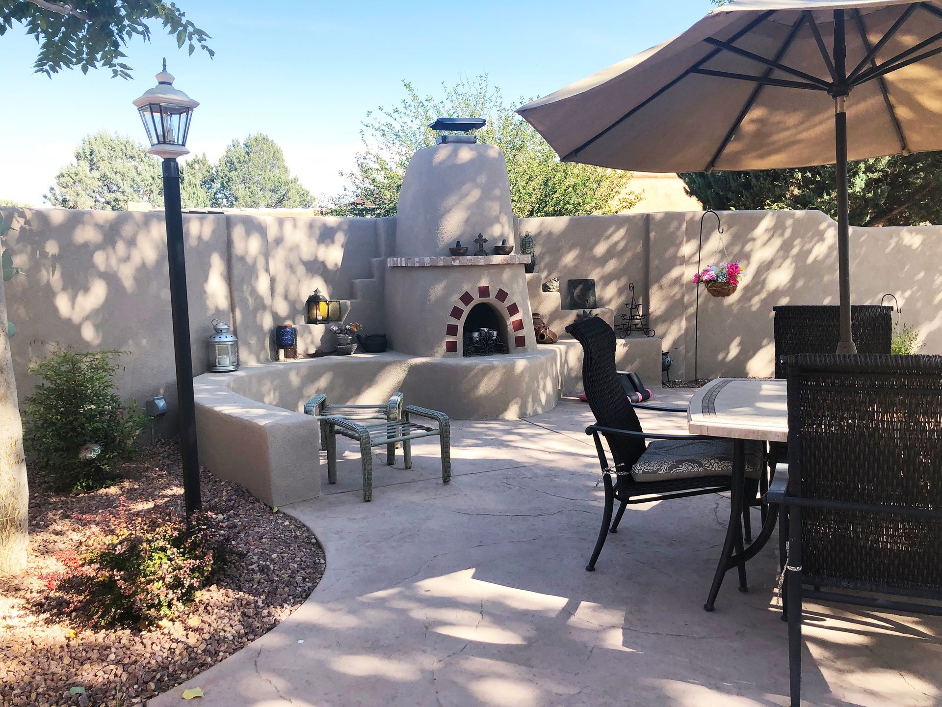 Outdoor patio with a stucco wall, outdoor oven, seating, and an umbrella.