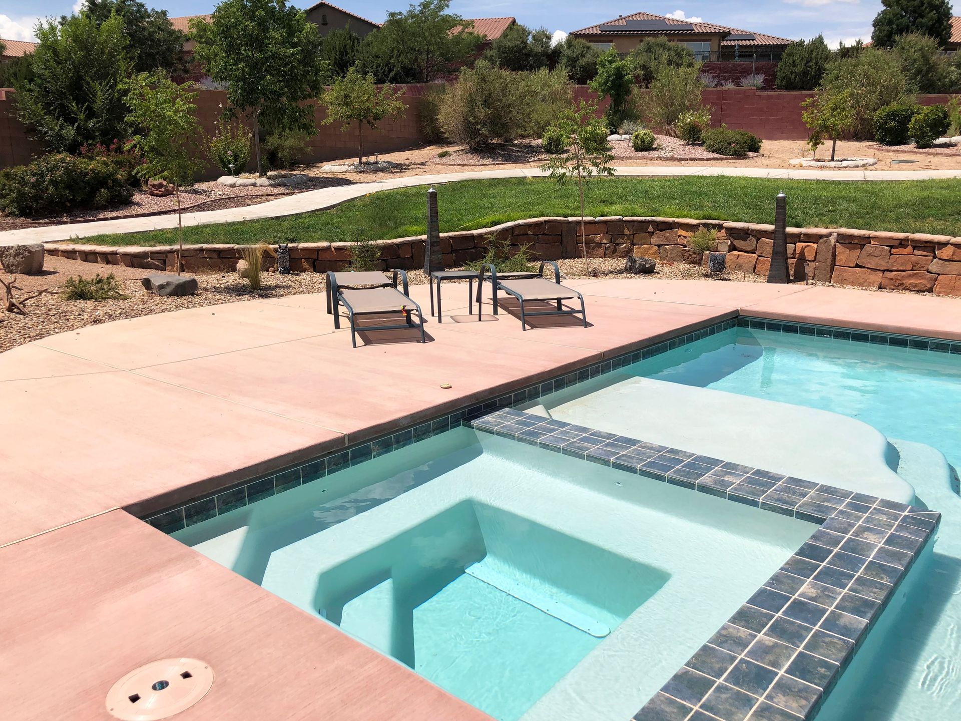 Pool with attached spa; lounge chairs on patio, green grass and trees in the background.