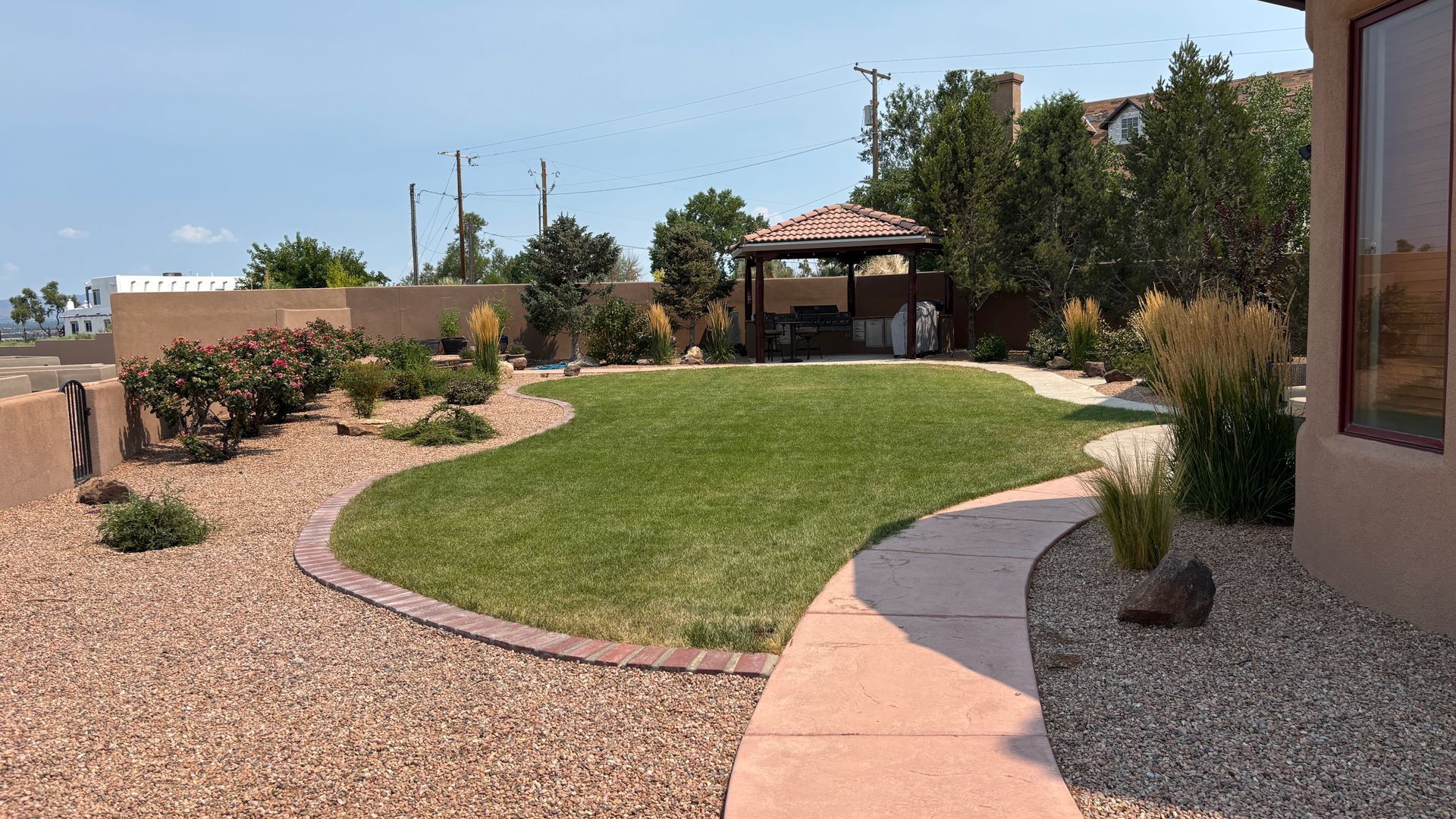 A well-manicured backyard with grass, rock landscaping, a pathway, and a shaded structure.