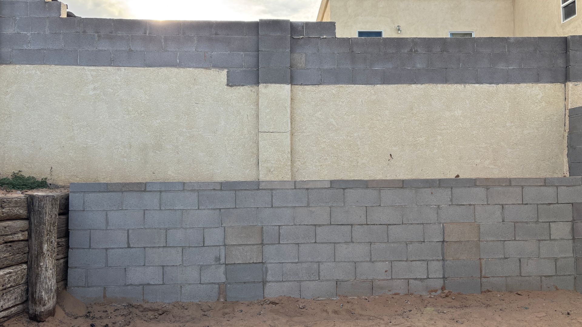 Gray block wall, retaining wall, light-colored stucco with a darker gray block top, outdoors.