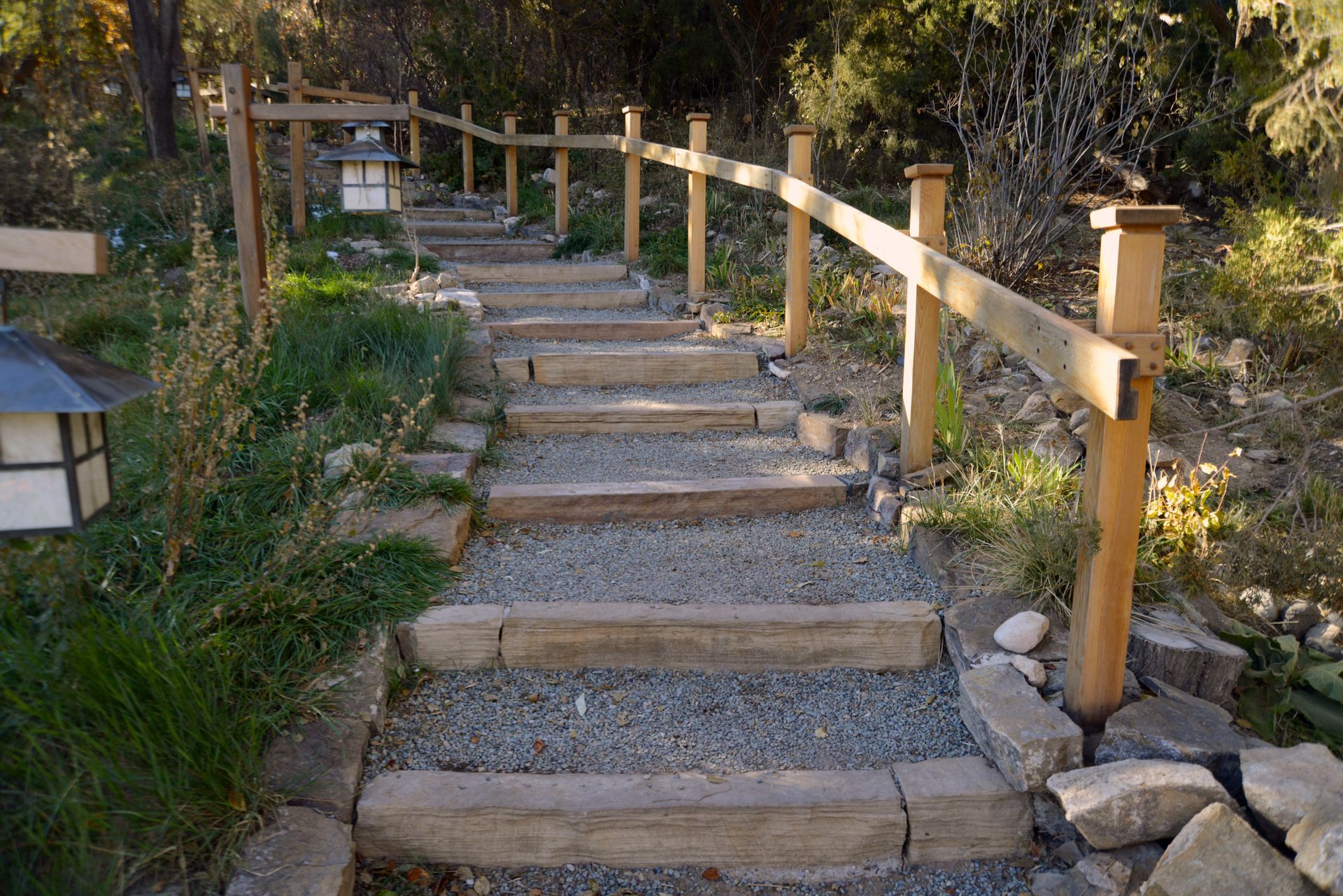 Wooden staircase with gravel steps and a wooden railing ascends through a garden.