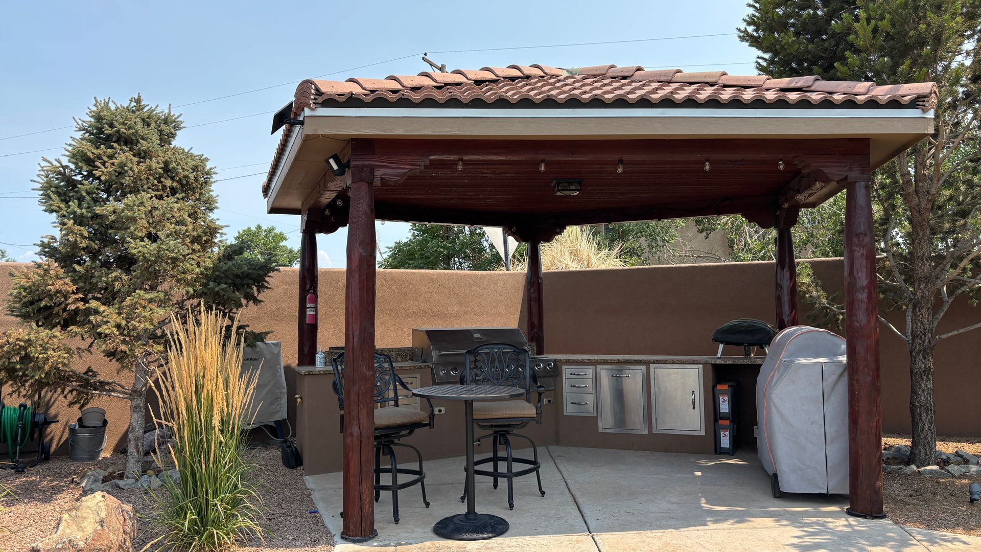 Outdoor kitchen with grill, seating, and counter under a covered pergola.