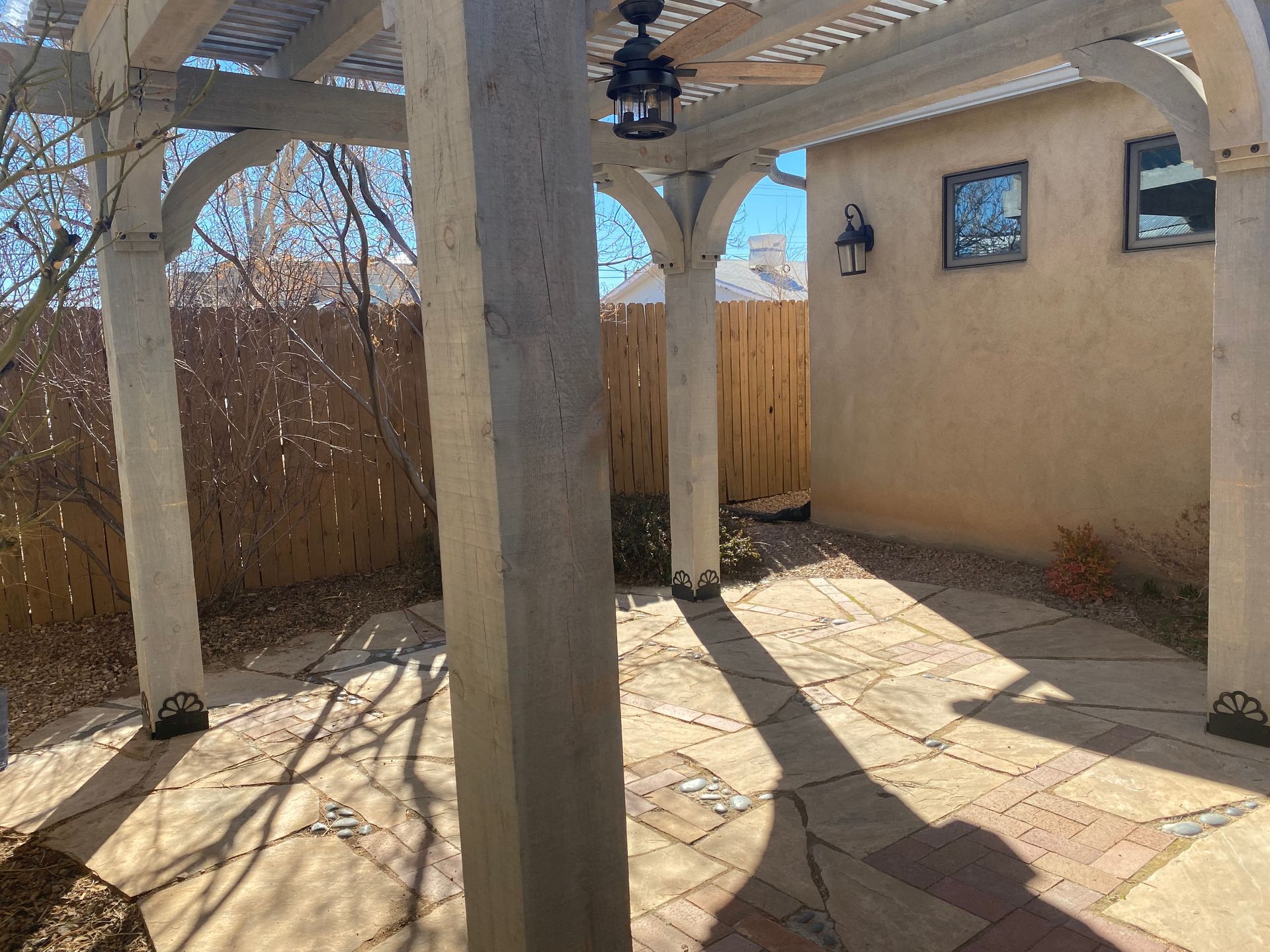 Courtyard with pergola and stone patio, tan stucco walls, and wooden fence.