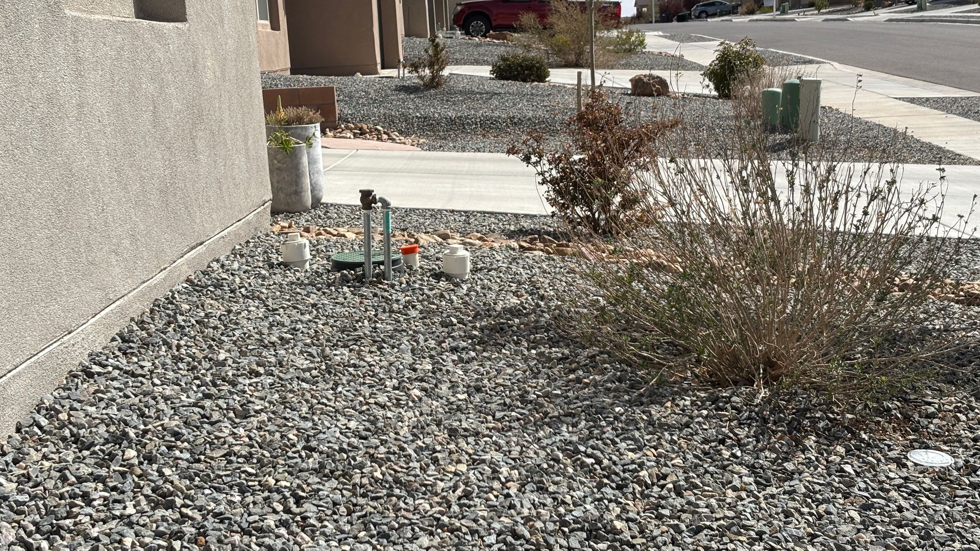 Gravel landscaping with a bush, concrete sidewalk, and a building.