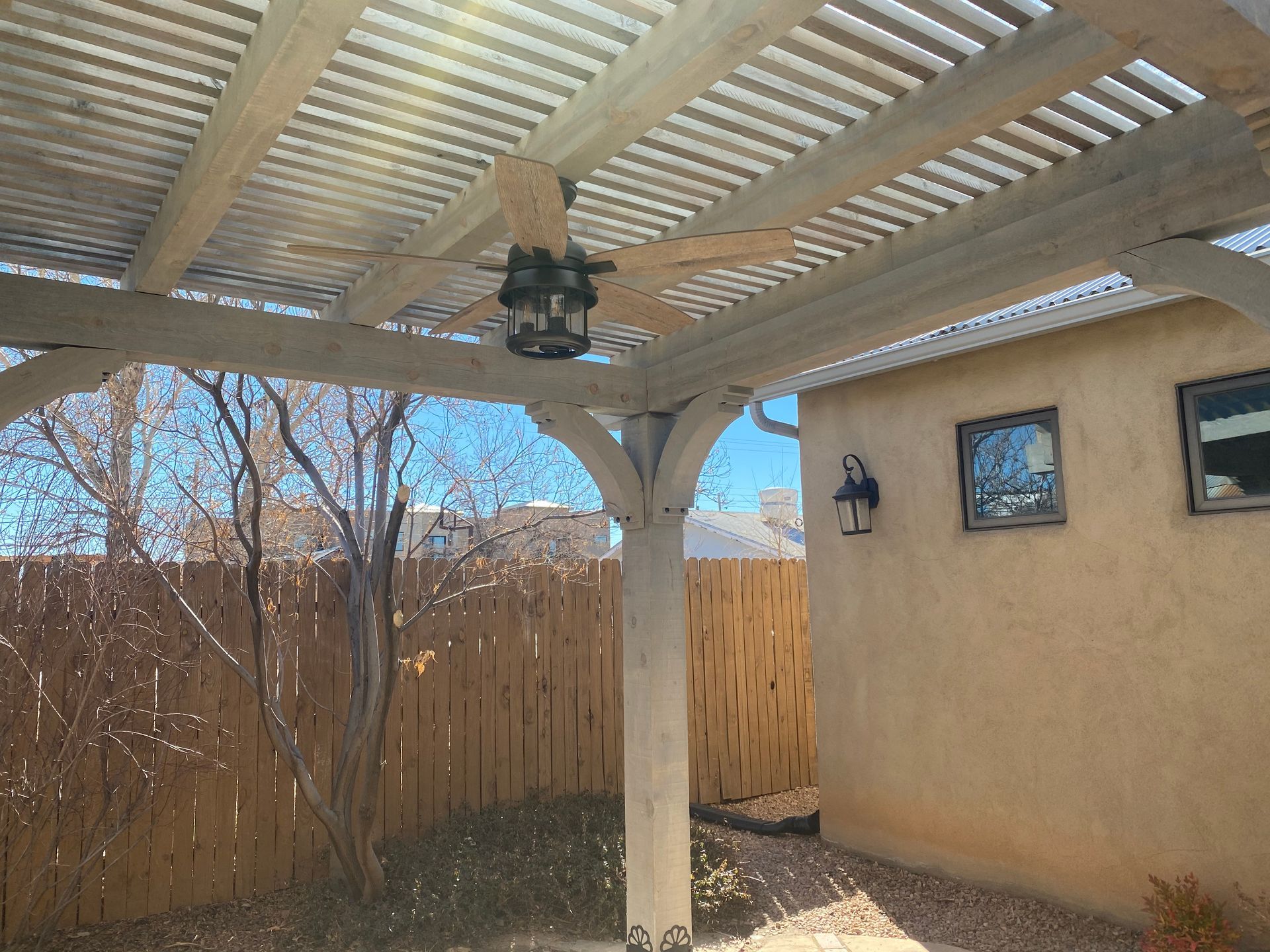 Outdoor patio with pergola, ceiling fan, and beige stucco wall.