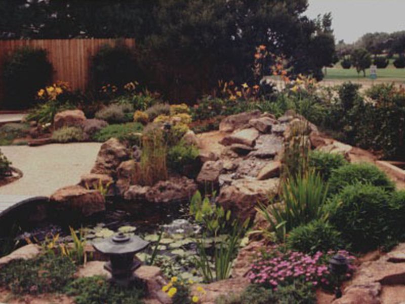 Rock garden pond with waterfall, stone path, and pink flowers in a landscaped backyard