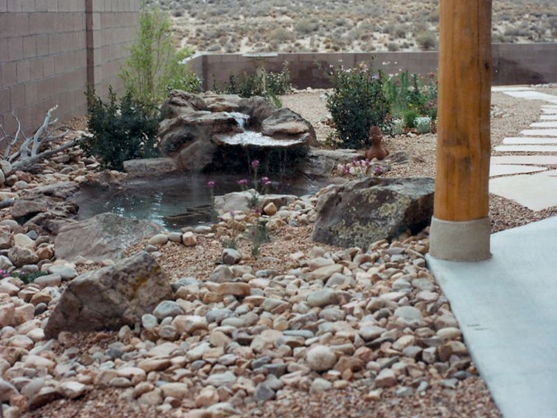 Backyard rock garden with a small waterfall and stream beside a concrete patio and wooden post