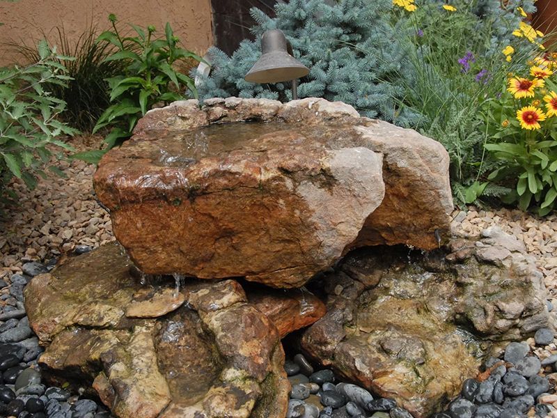 Stacked rocks forming a garden sculpture with flowers and greenery in the background