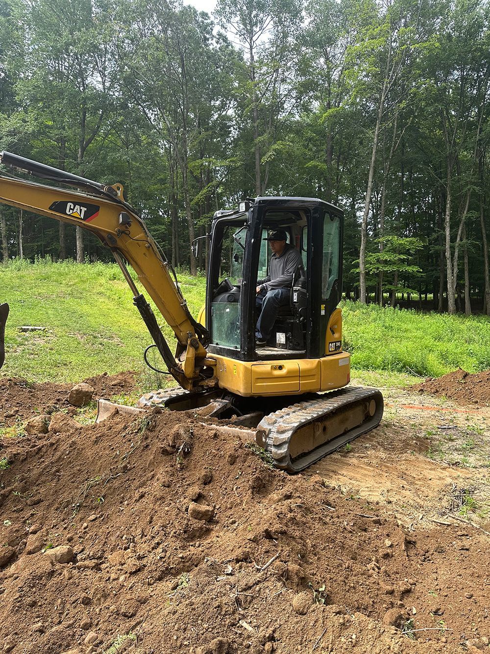 A man is driving a mini excavator in a dirt field