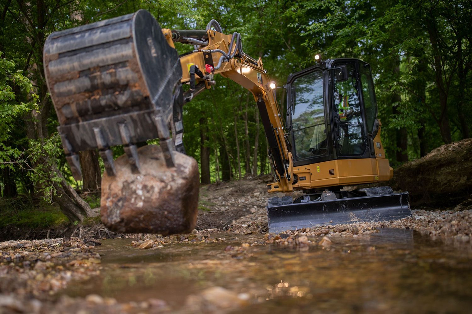 A small excavator is digging a stream in the woods