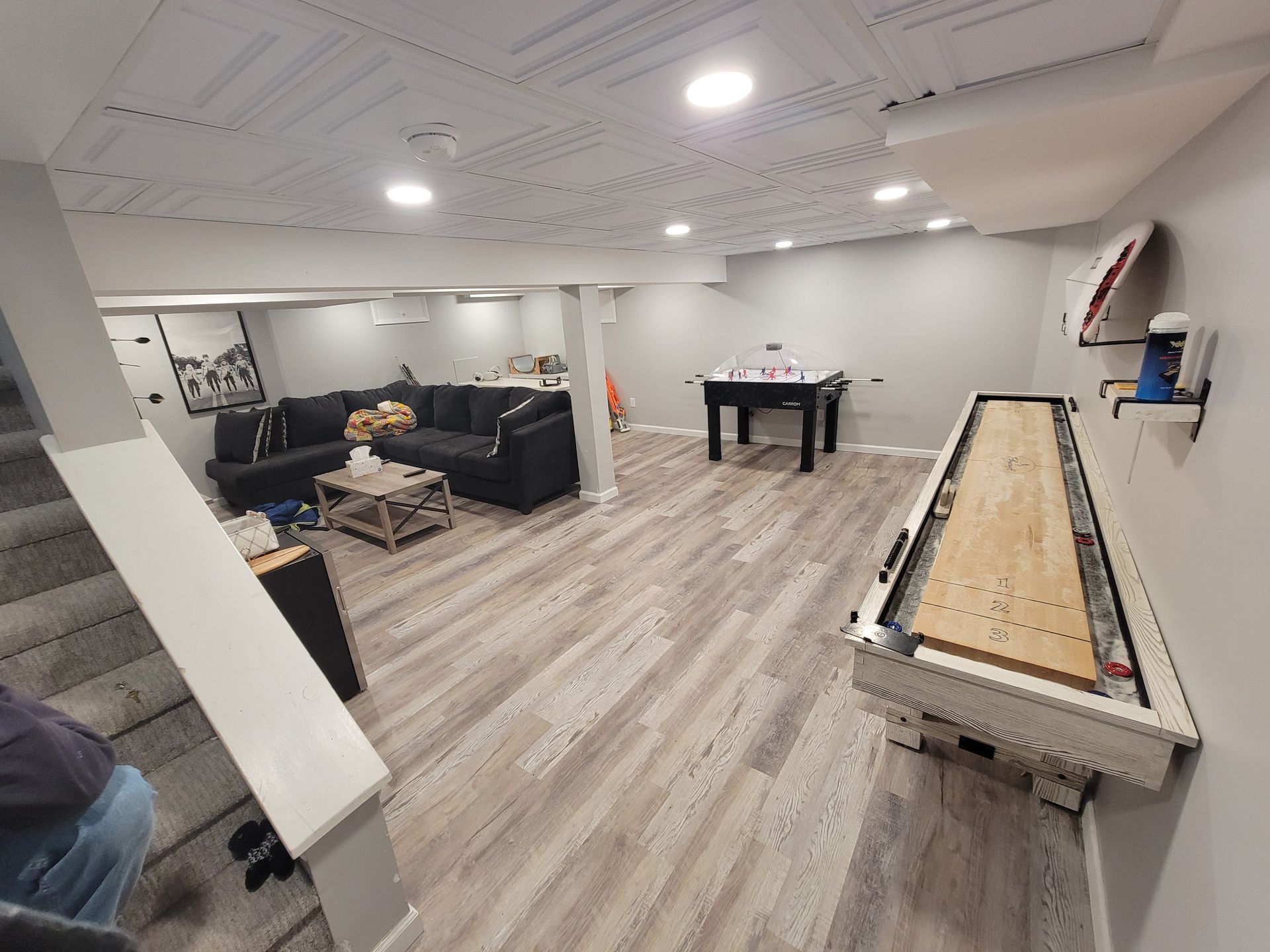 A living room in a basement with a shuffleboard table and a couch.