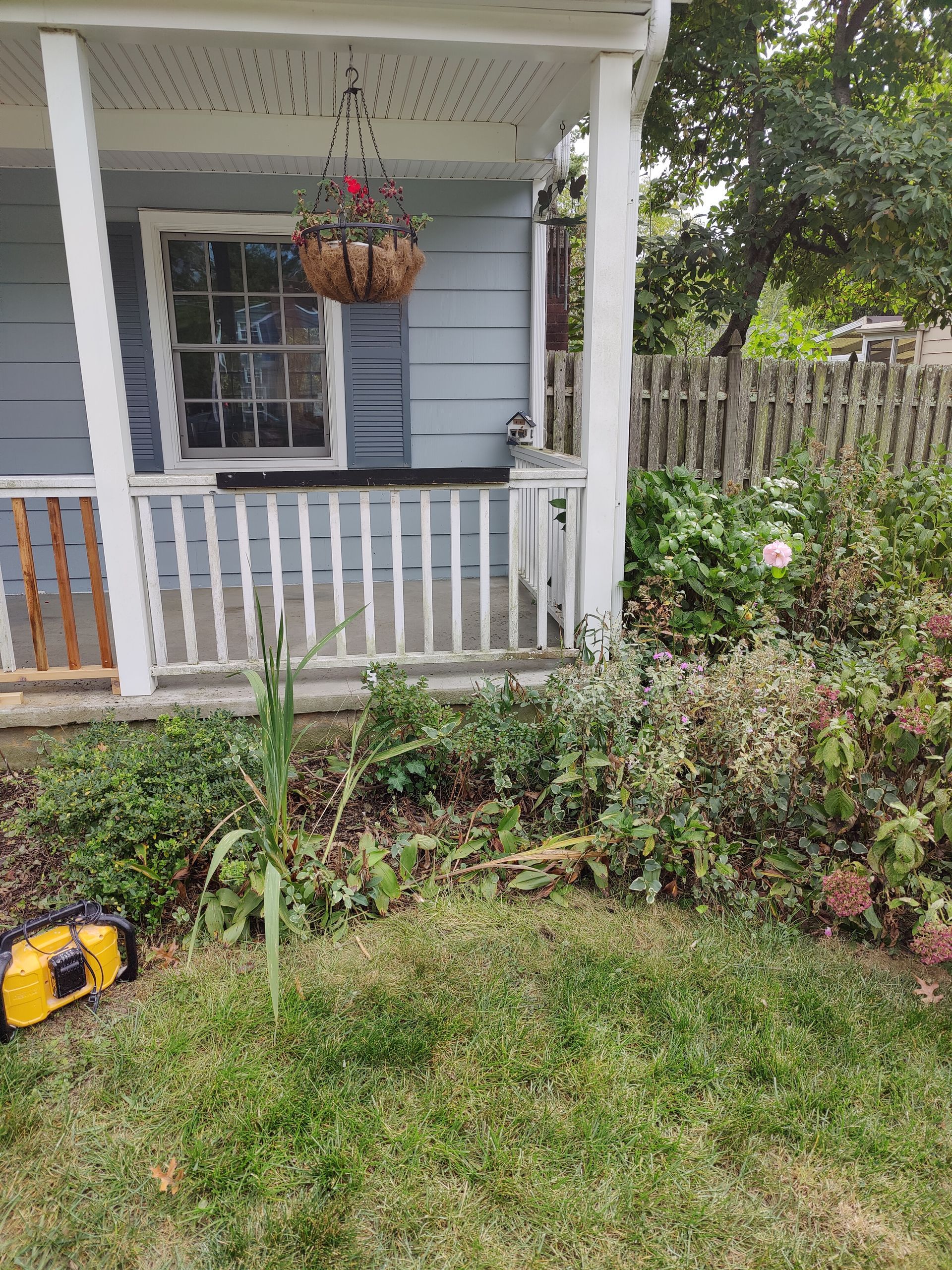 A house with a porch and a lawn mower in front of it.