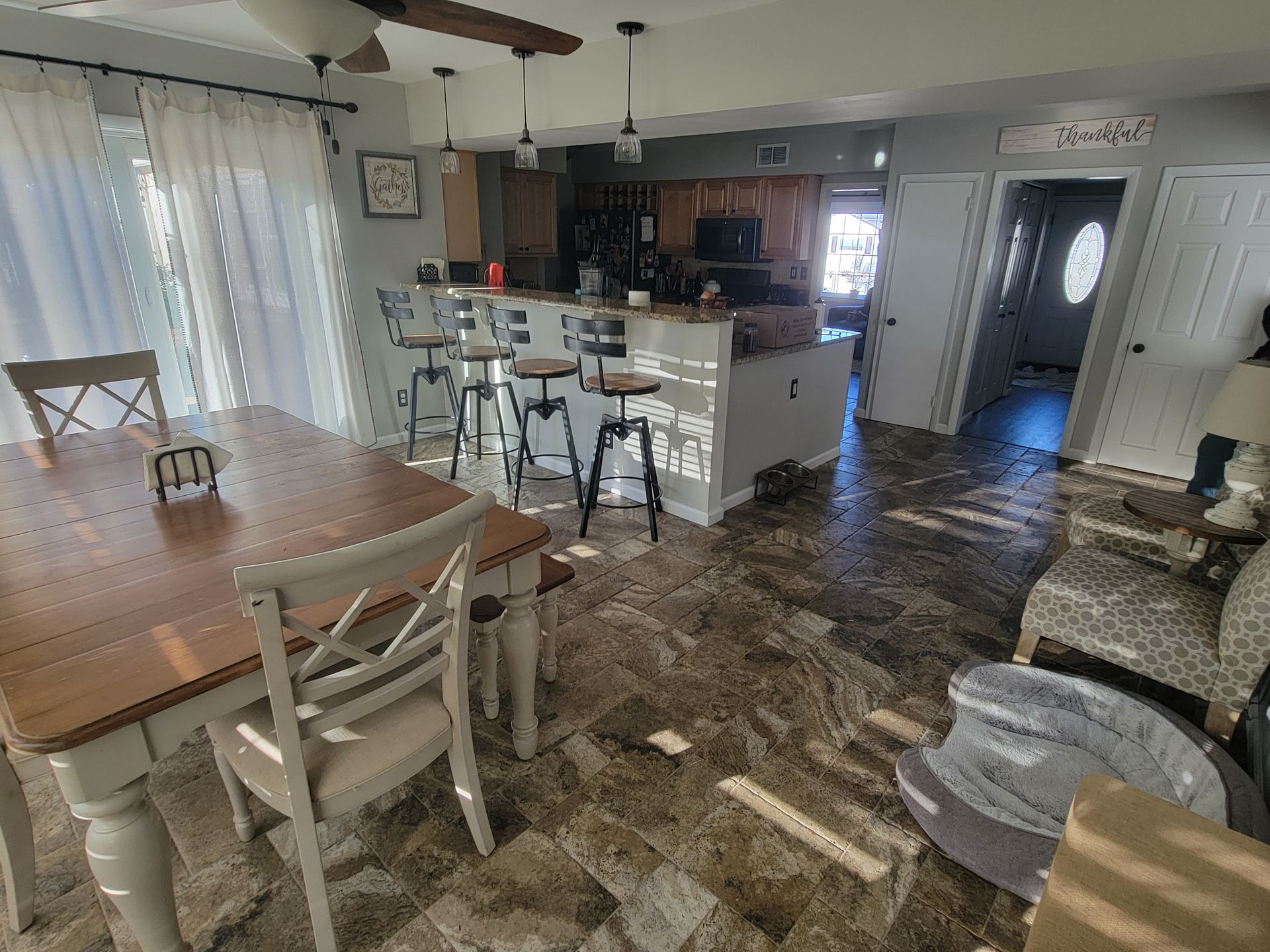 A dining room with a table and chairs and a kitchen in the background.