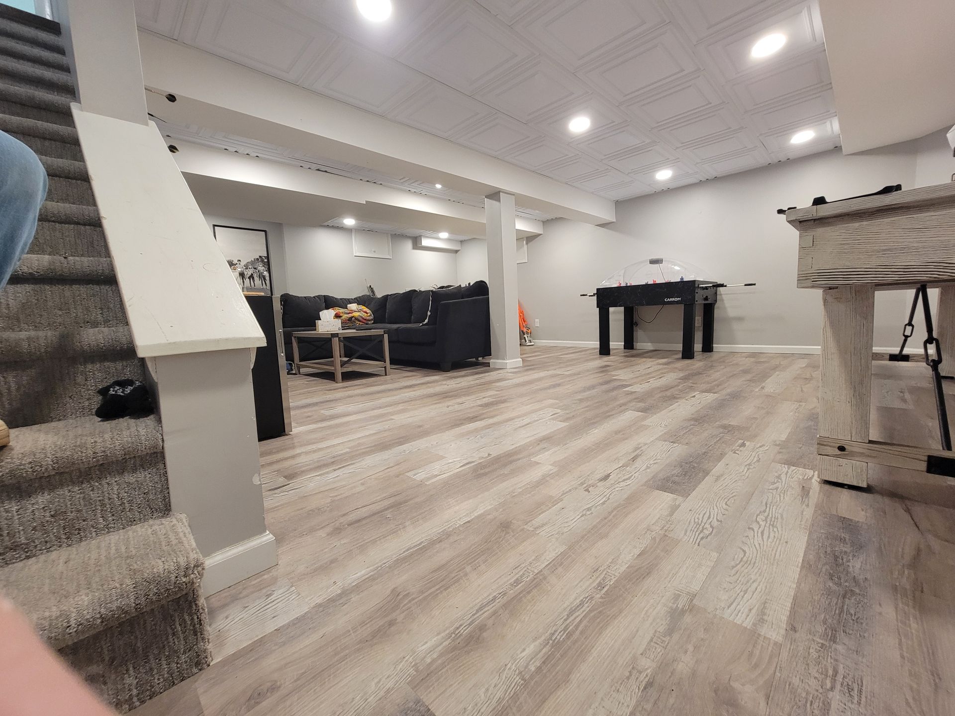A basement with hardwood floors, a couch, a table, and stairs.