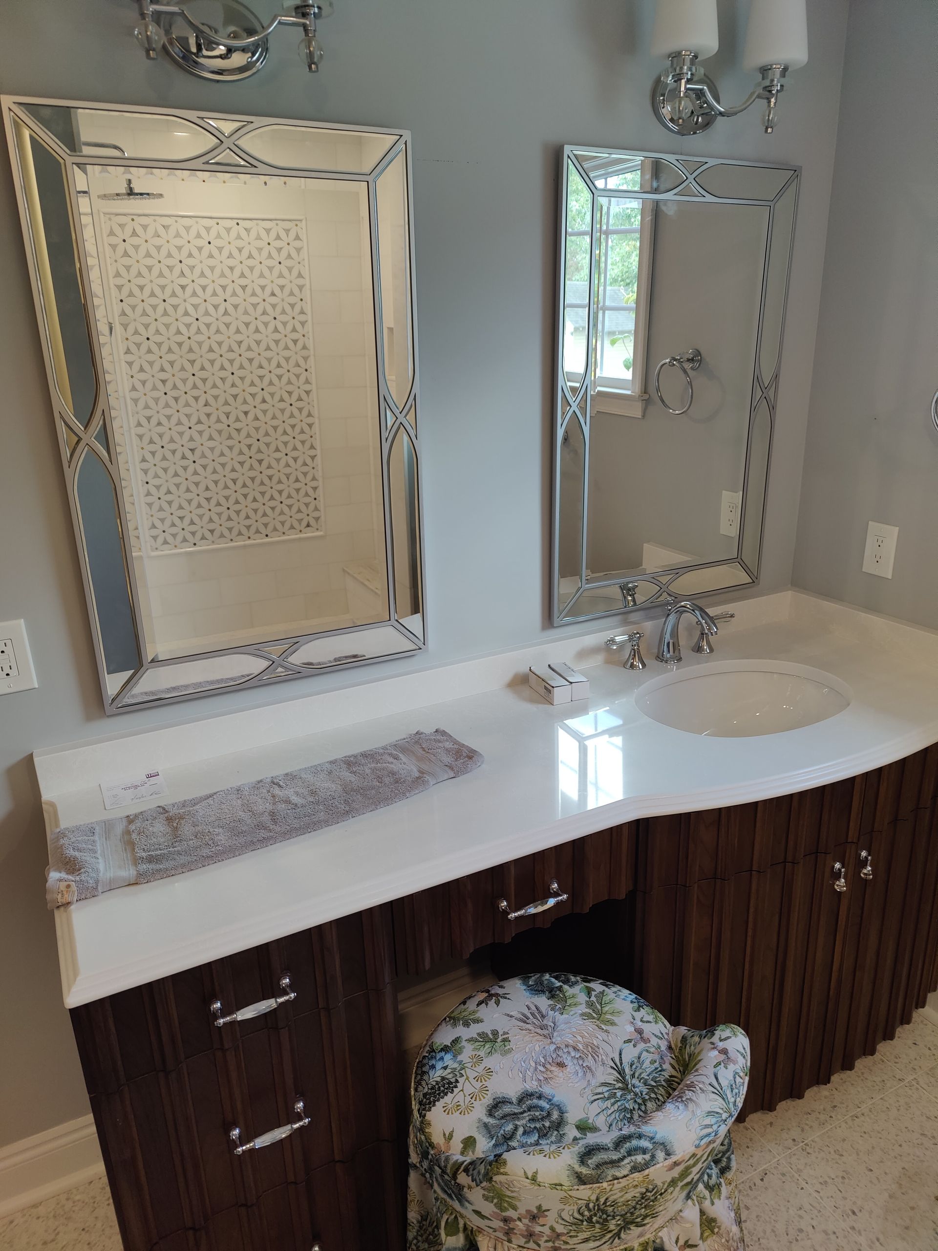 A bathroom with two mirrors , a sink , and a stool.