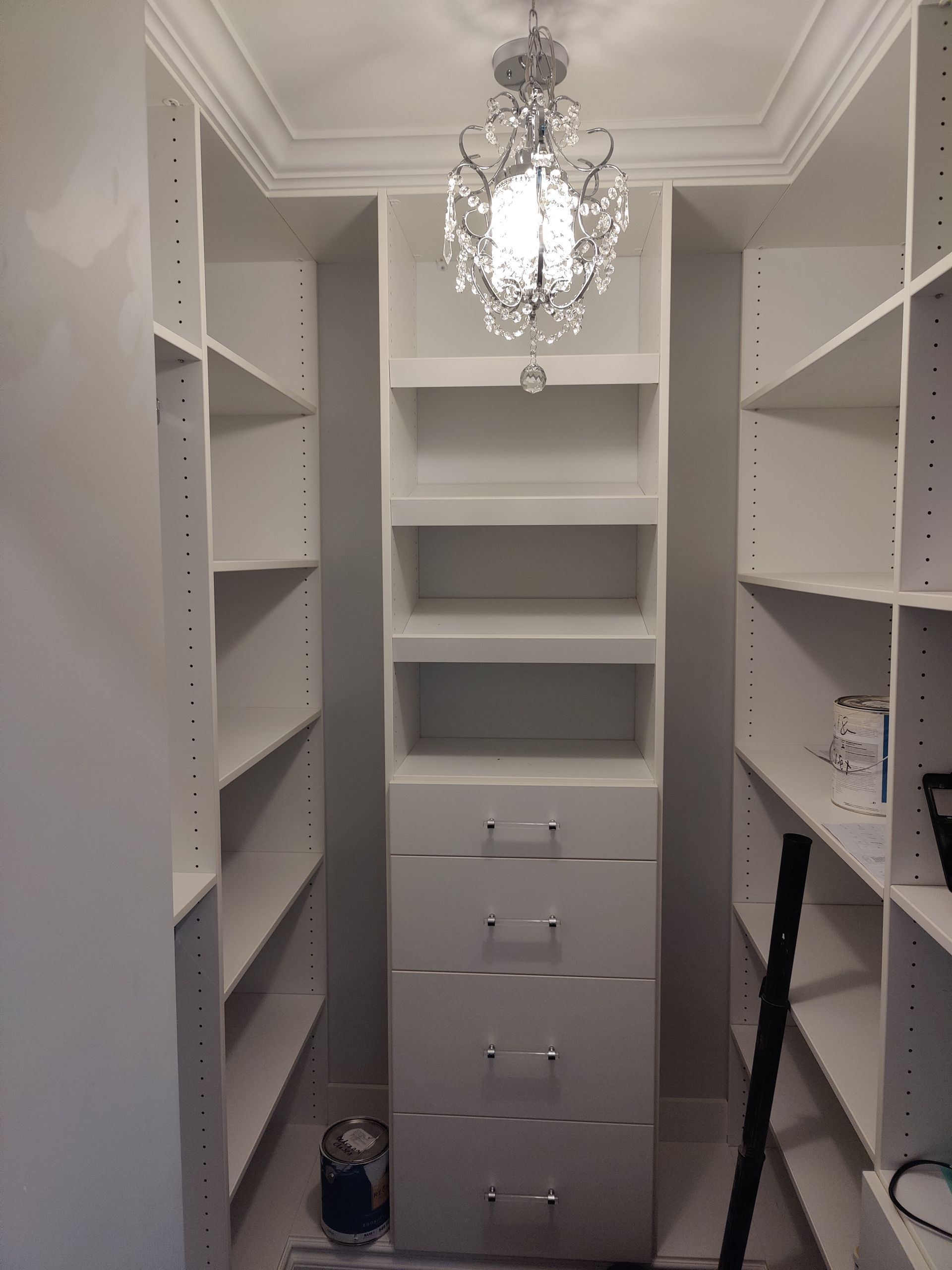A walk in closet with lots of shelves and drawers and a chandelier hanging from the ceiling.