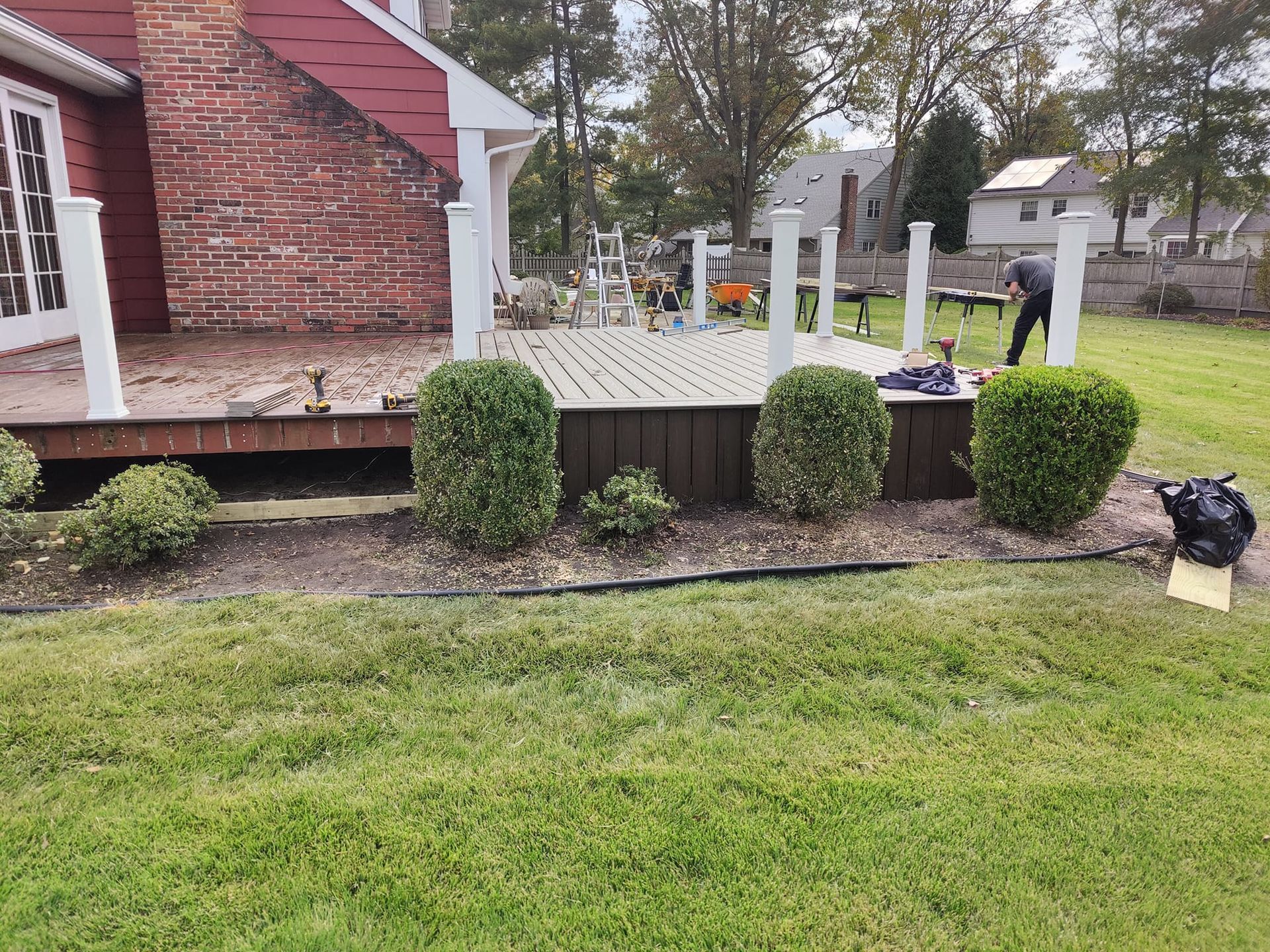 A man is working on a deck in the backyard of a house.
