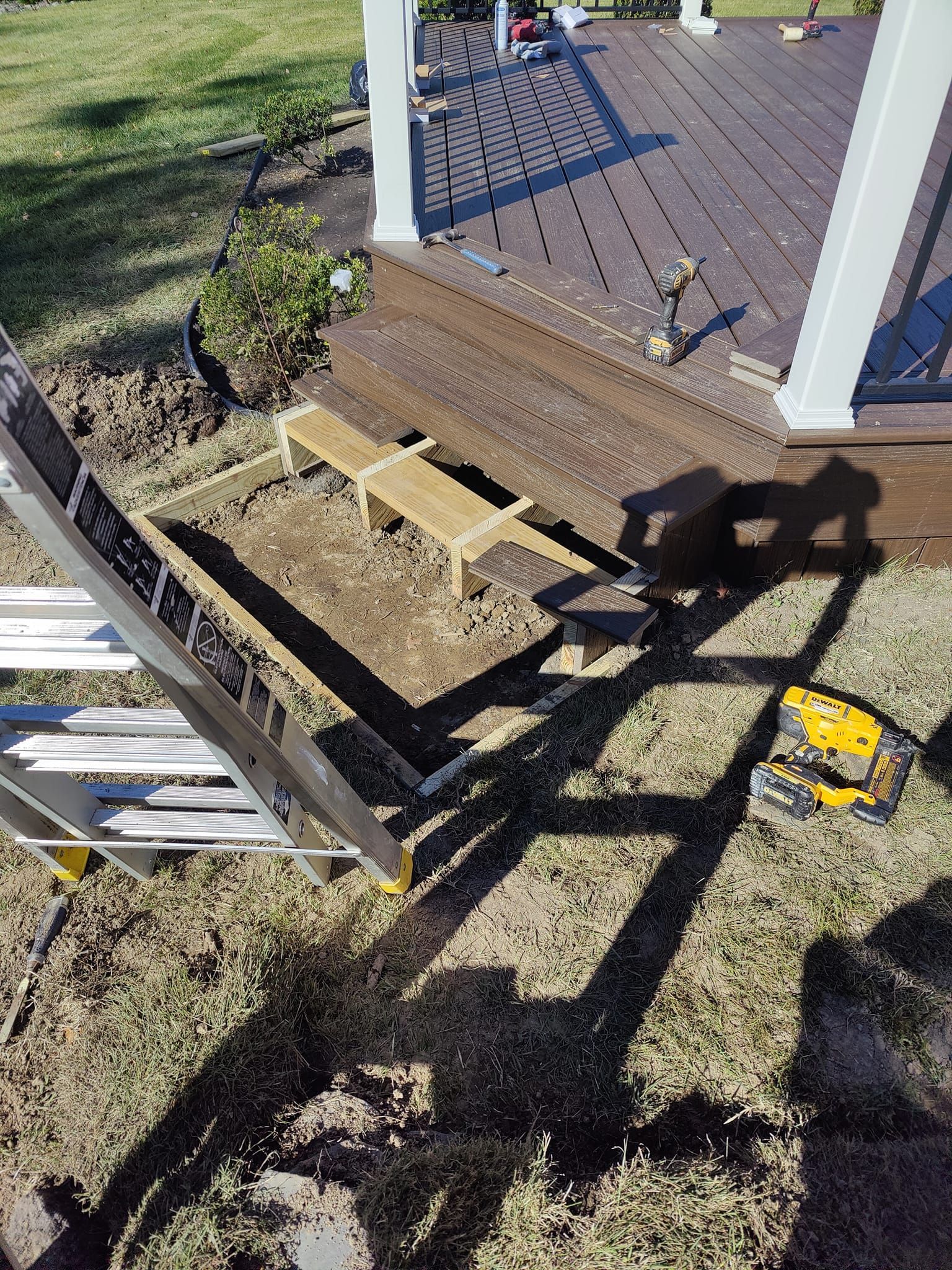 A ladder is sitting on the ground next to a wooden deck.