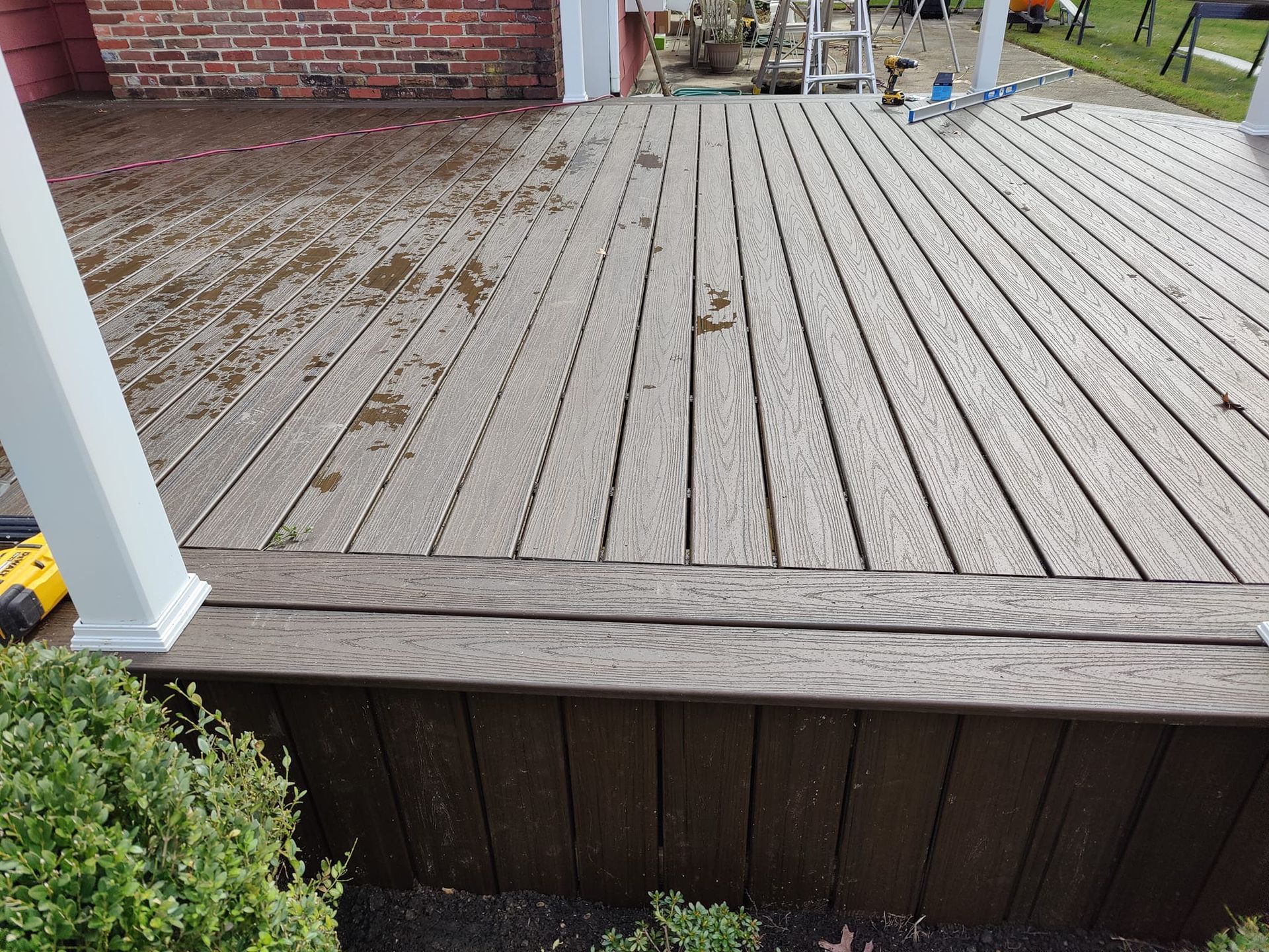 A wooden deck with a white railing and a brick wall in the background.