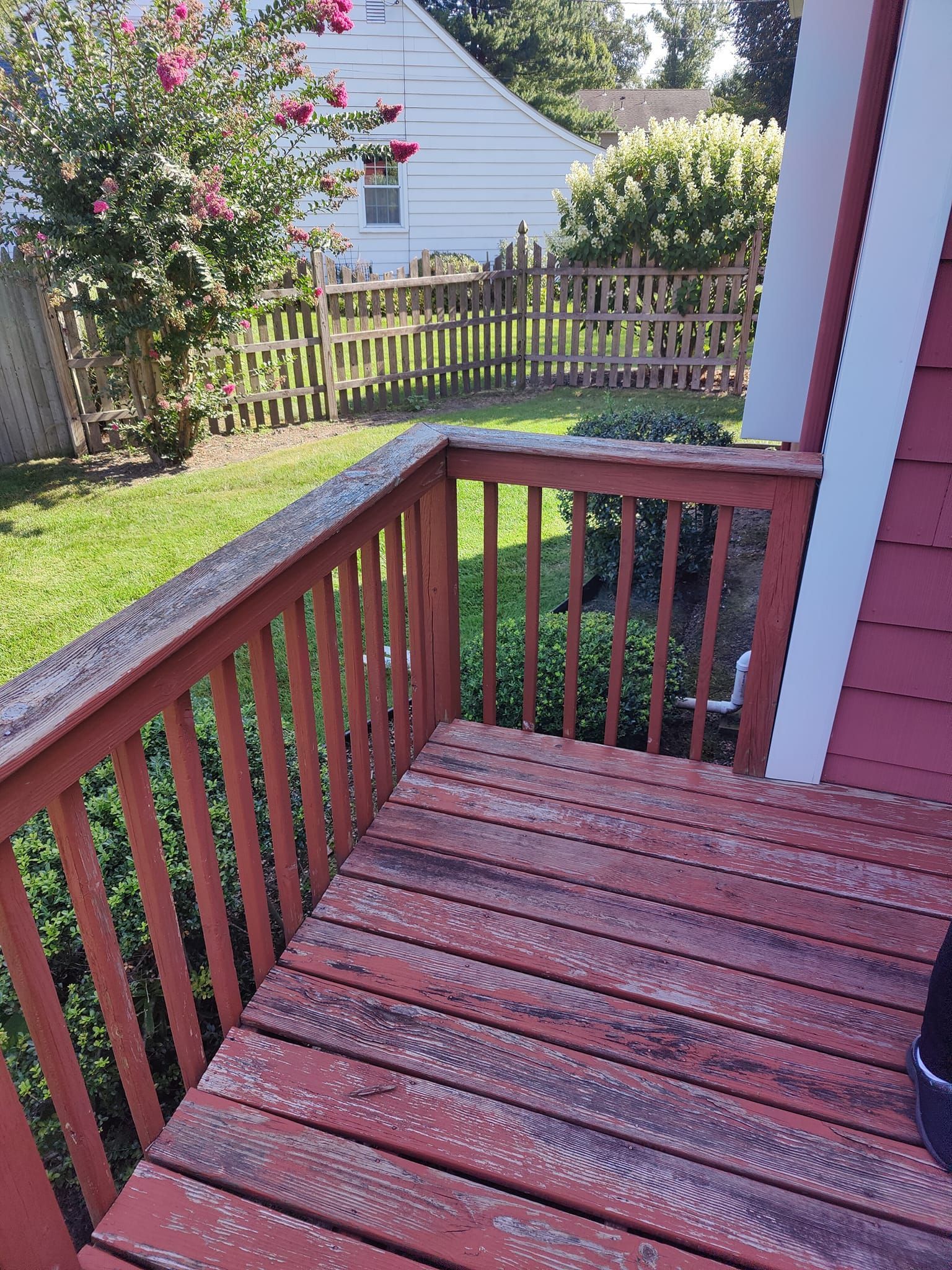 A wooden deck with a fence in the background and a house in the background.