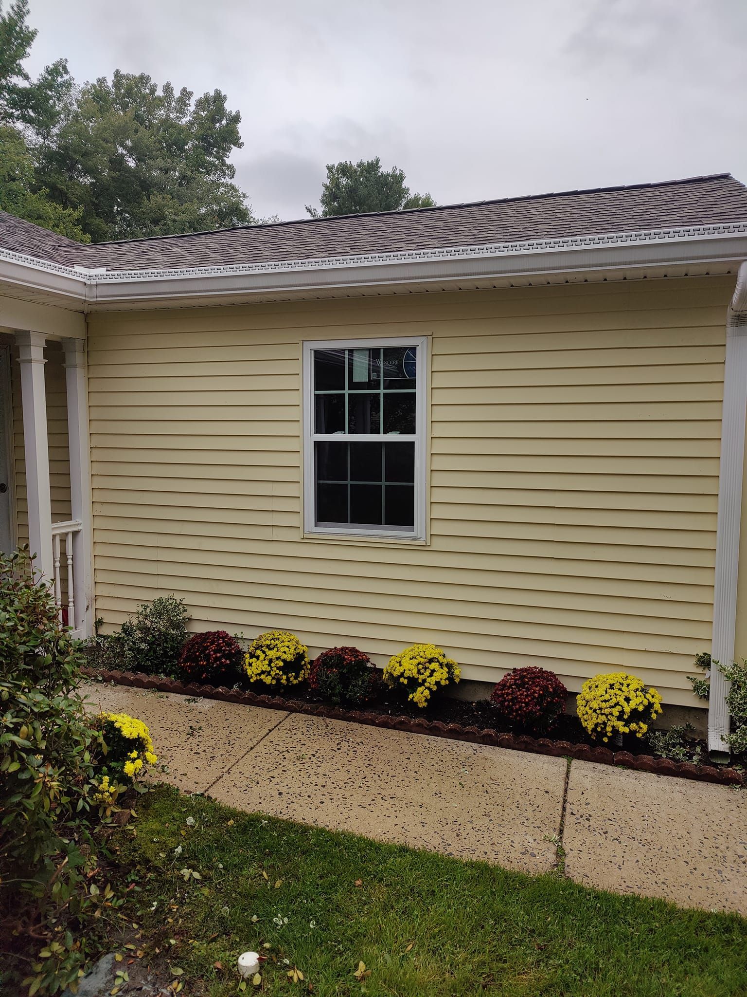 A yellow house with a window and flowers in front of it.