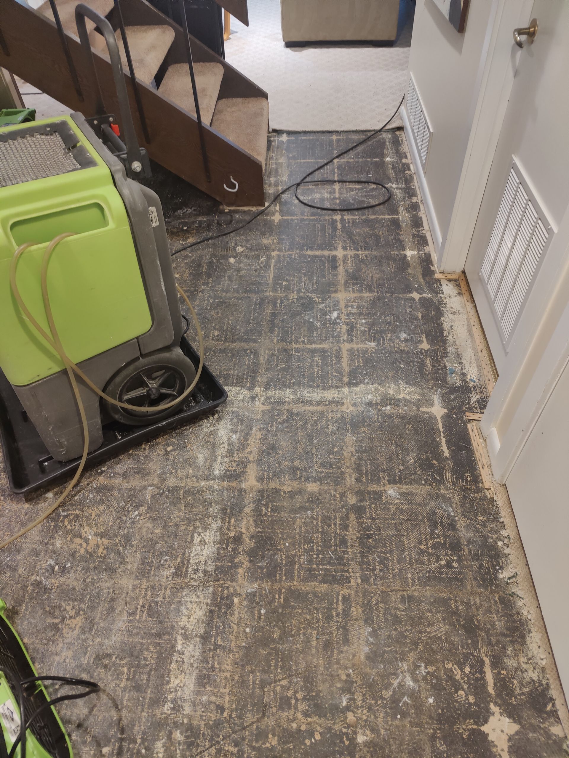 A green vacuum cleaner is sitting on a tiled floor next to a staircase.