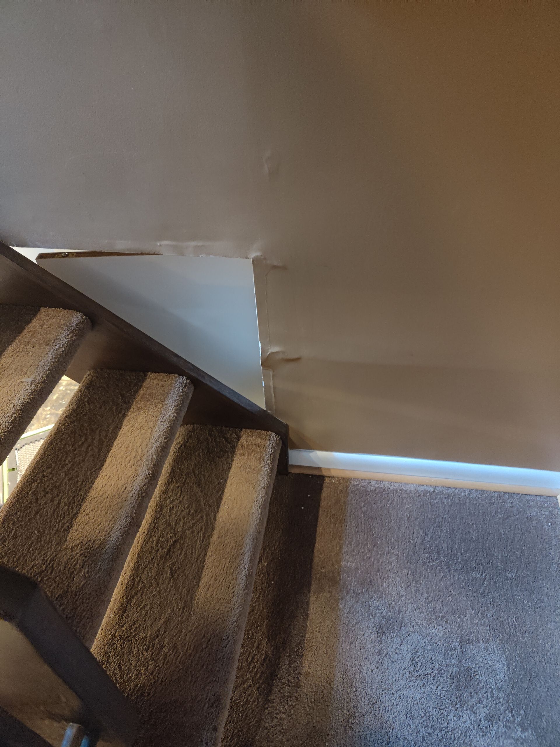A staircase with a carpeted landing and a broken wall.