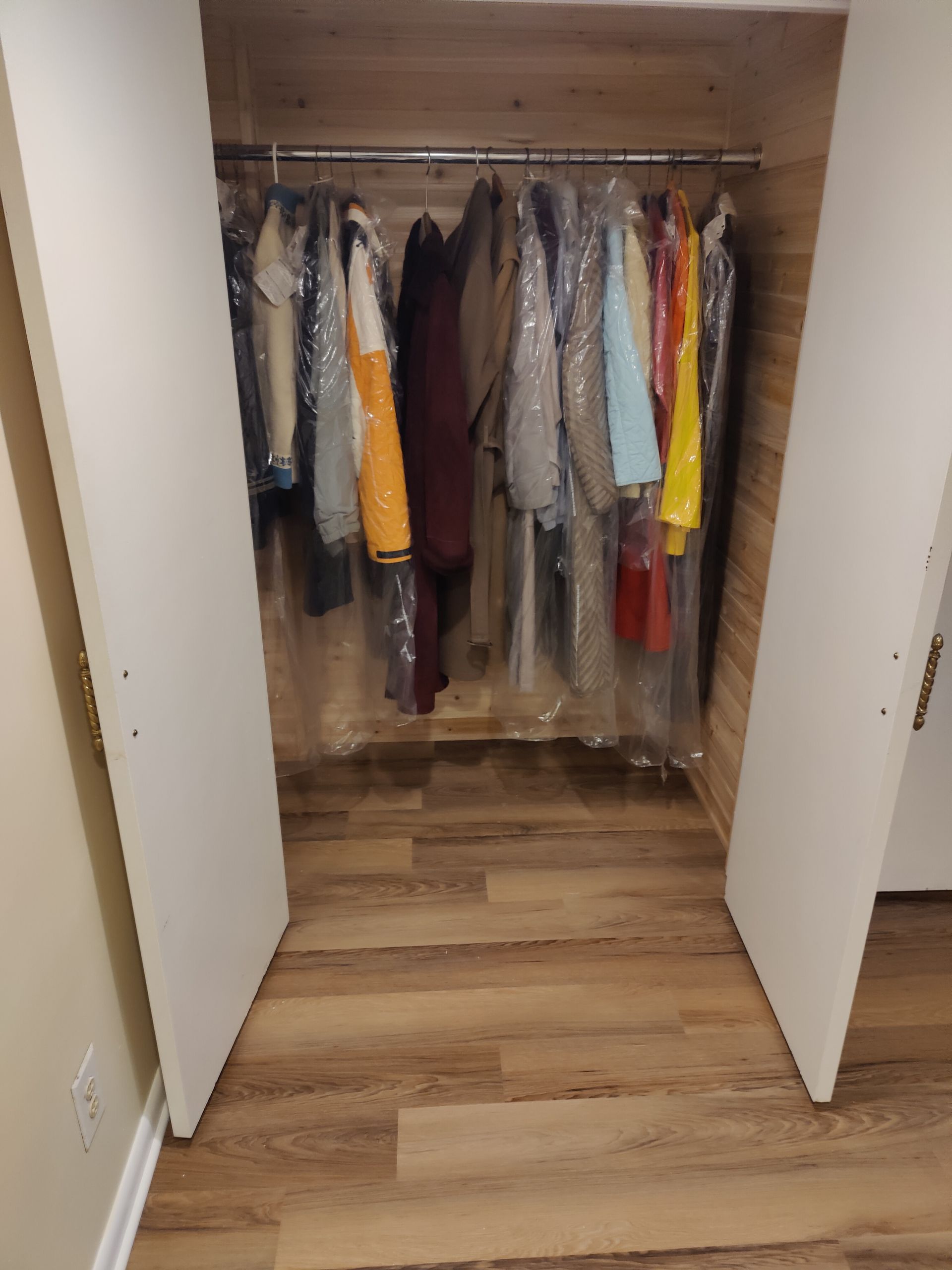 A closet filled with clothes wrapped in plastic bags.