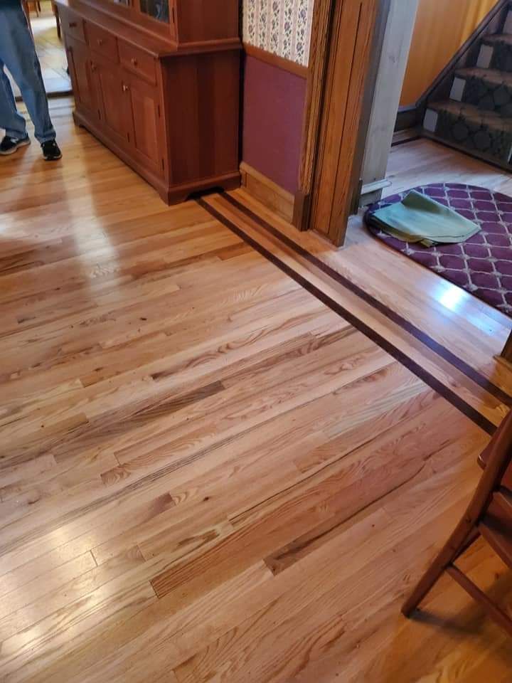 A wooden floor in a room with a dresser and stairs.