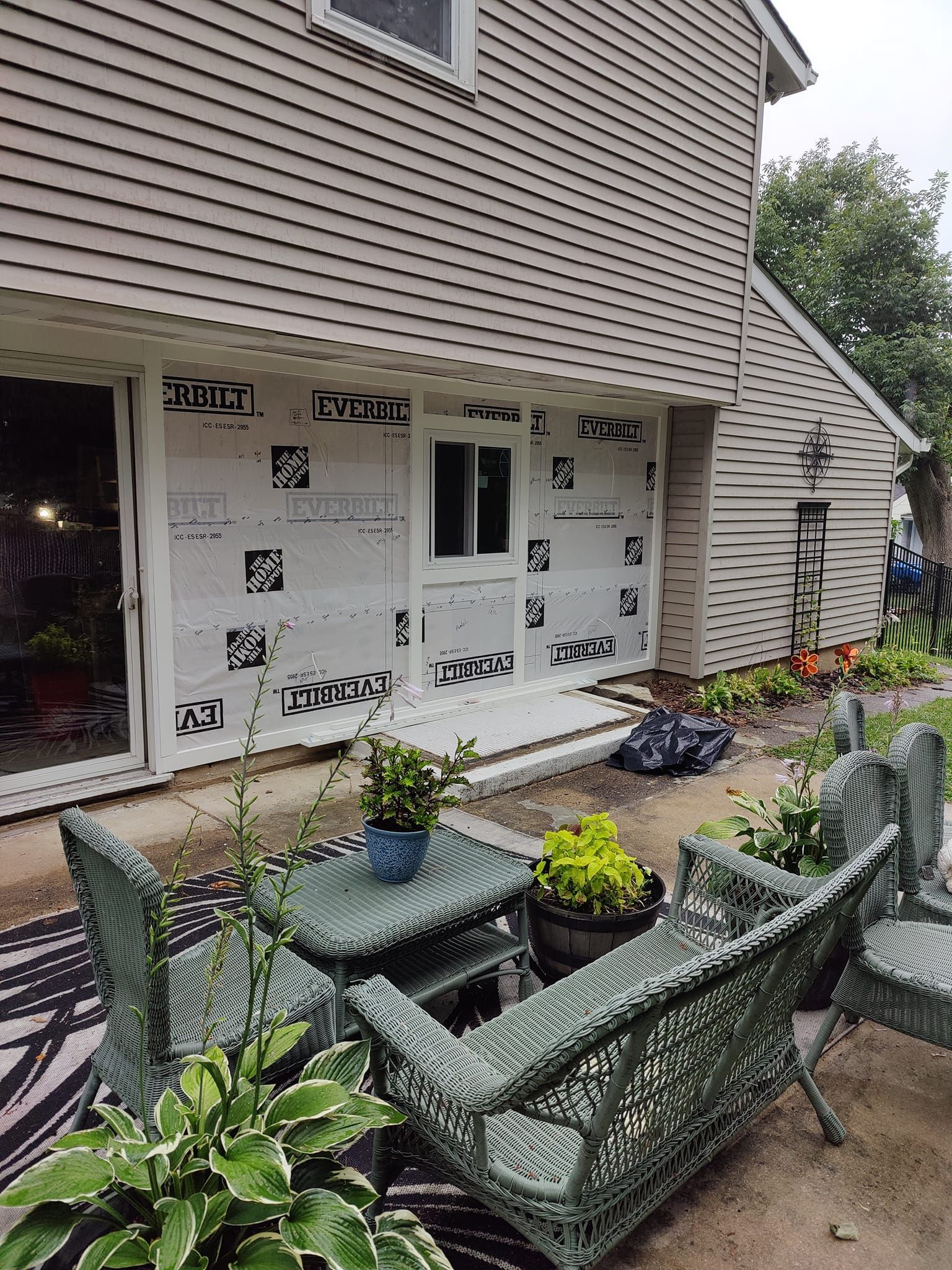 A patio area with a couch , chairs , tables and potted plants in front of a house.