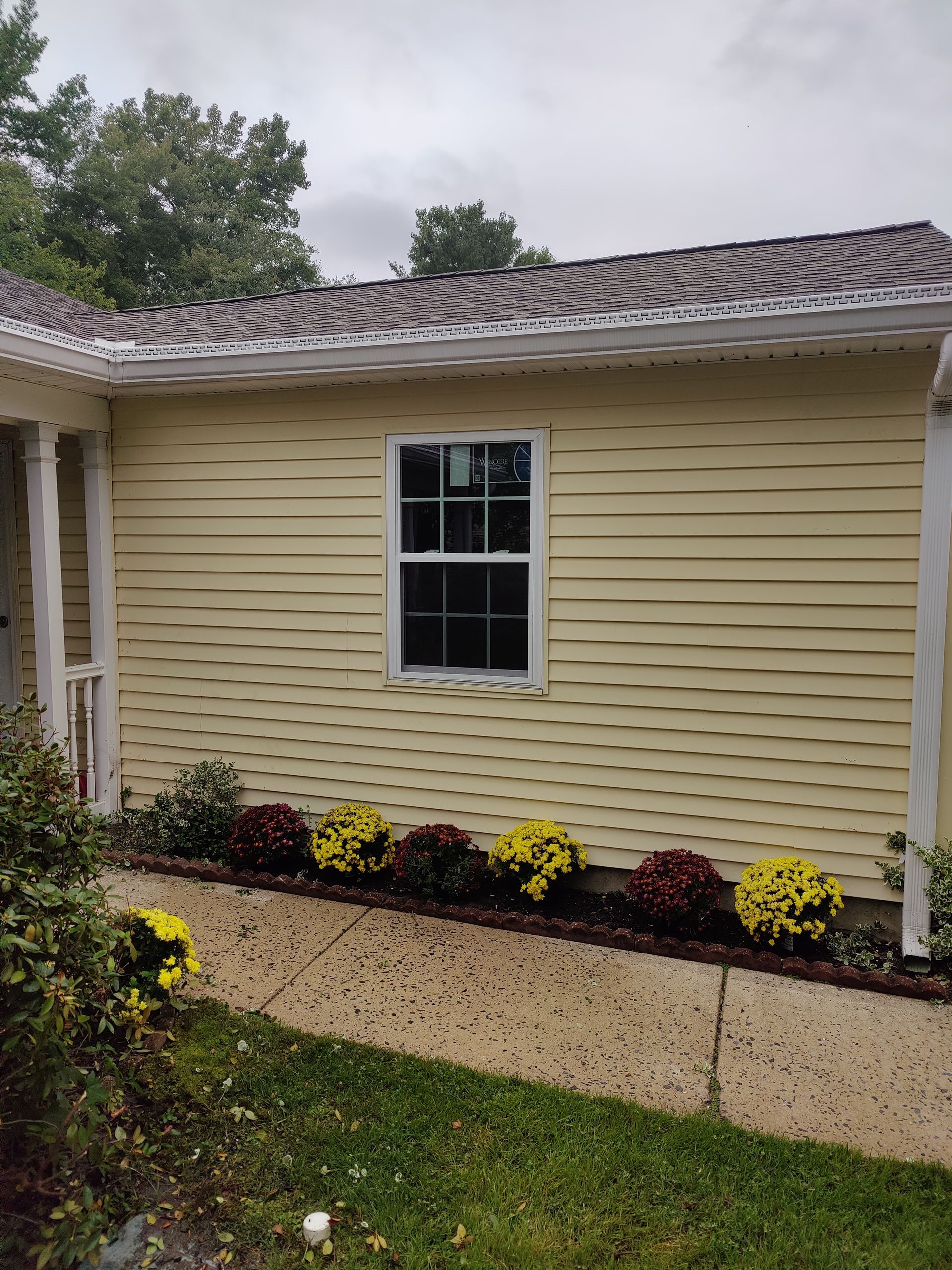 A yellow house with a window and flowers in front of it.