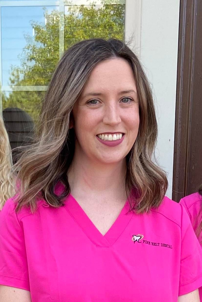 Woman in pink scrubs smiles, outdoors.